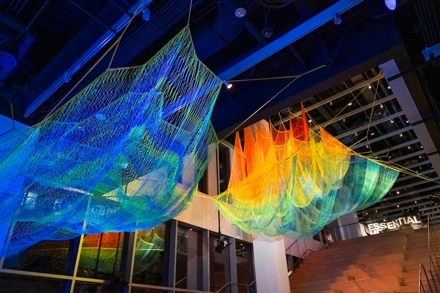 A colourful artwork in blue, green, red, yellow and blue hanging from ceiling and just above the staircase