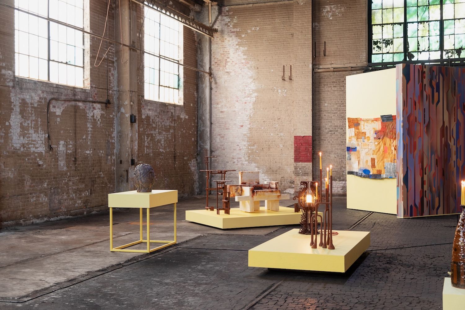 An exhibition set up with rustic walls and yellow plinths and furniture