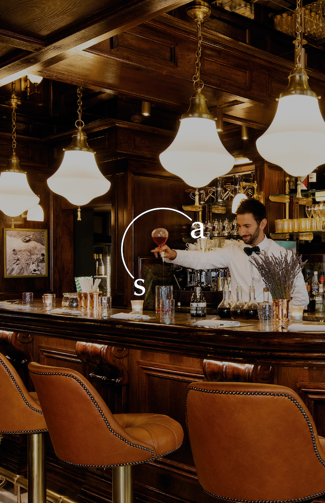 A bar with four lights and seats with bar tender serving drinks on the bar and a logo in the foreground