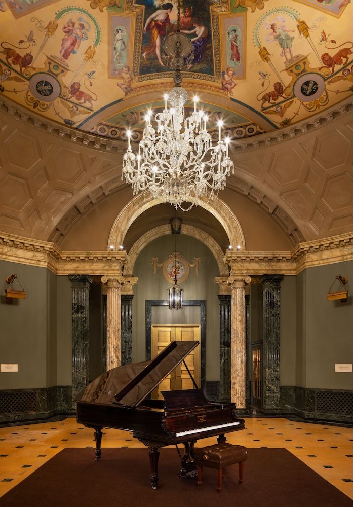 Grand piano at the centre of a room with chandelier hanging over it 