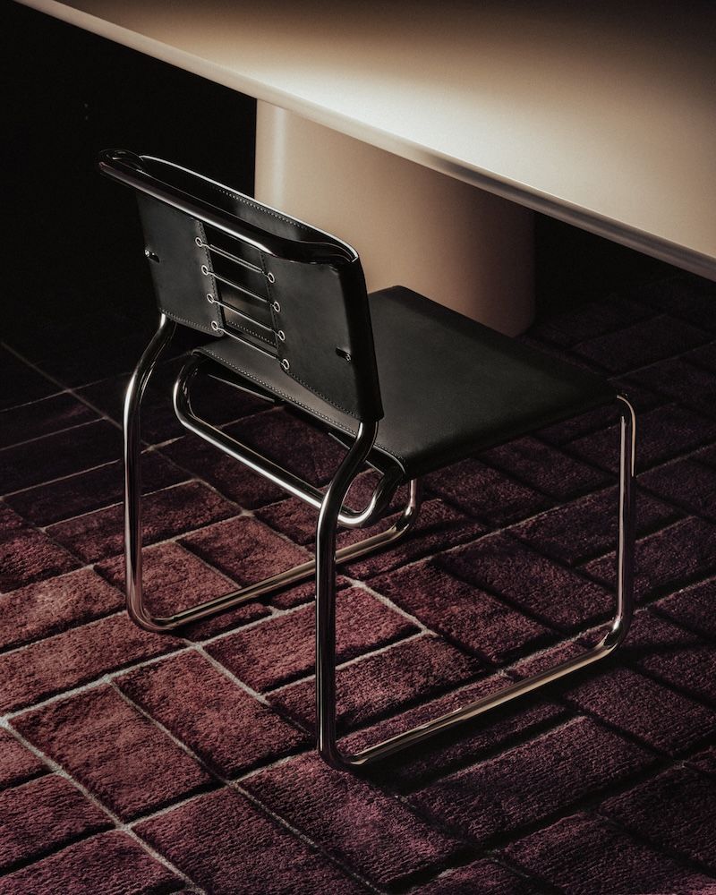 The back of a black chair with a backrest and metal legs on a carpeted ground
