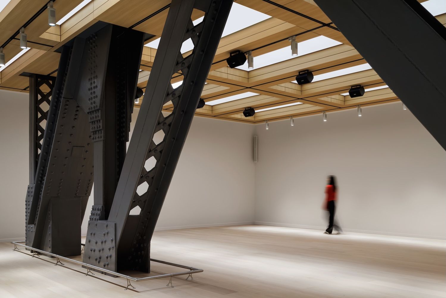 Structure of building with black steel legs and wall sky lights and figure walking through 