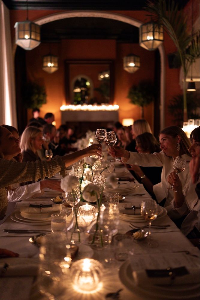 A crowd at a dimly lit dinner sitting at the table lit by candlelight and lanterns hanging above 