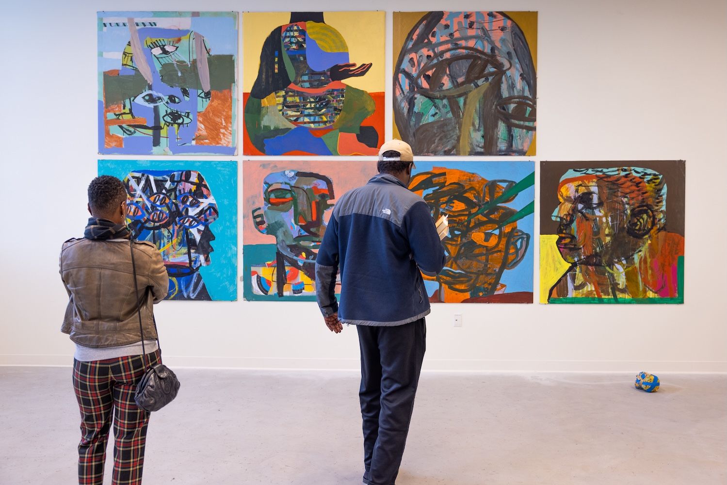 Artworks on the wall with two men looking at them 