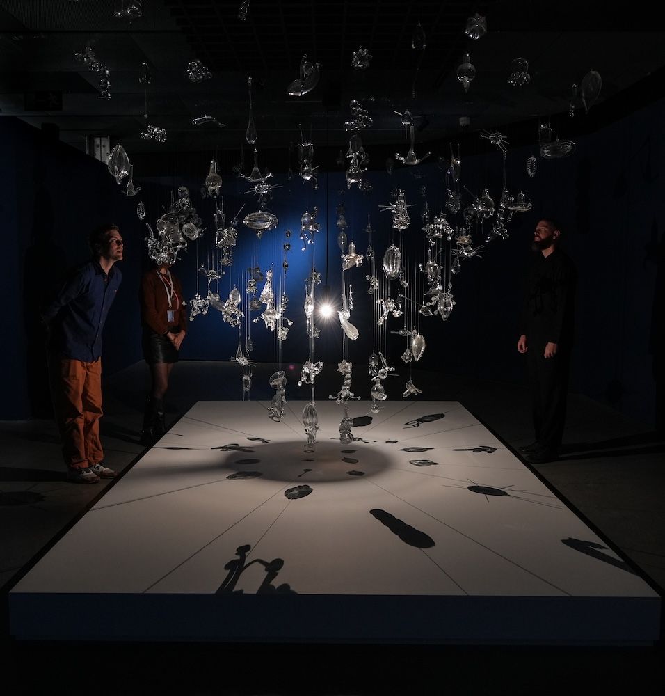Hanging glass pieces in a dark setting with shadows on the base 