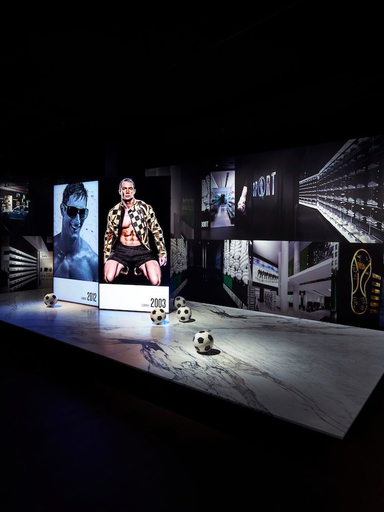 Dark exhibition setting with footballs in the foreground and imagery of men