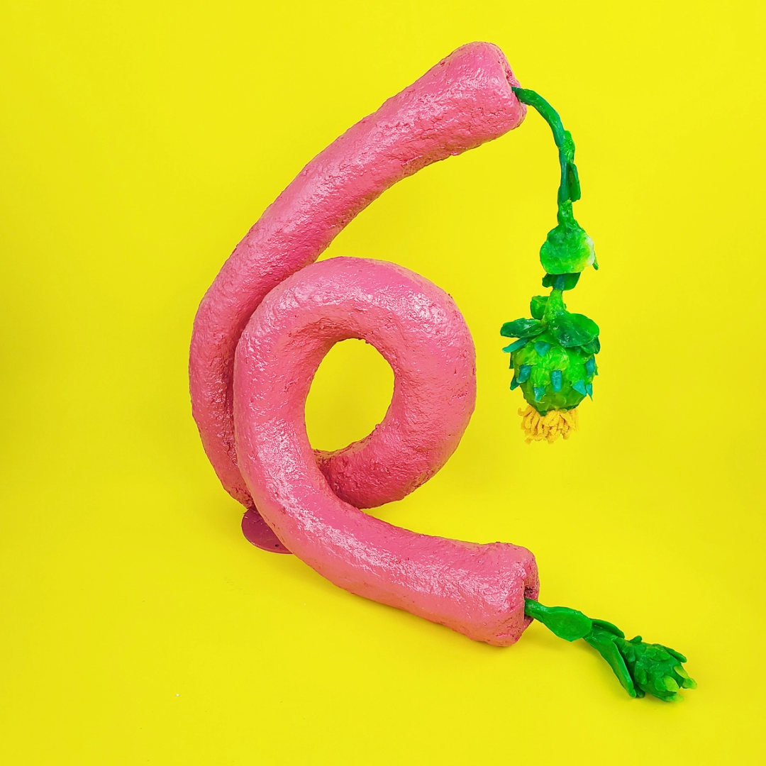 A bright pink sculpture of a curled tube with plant shaped objects coming out of both ends of the tube.