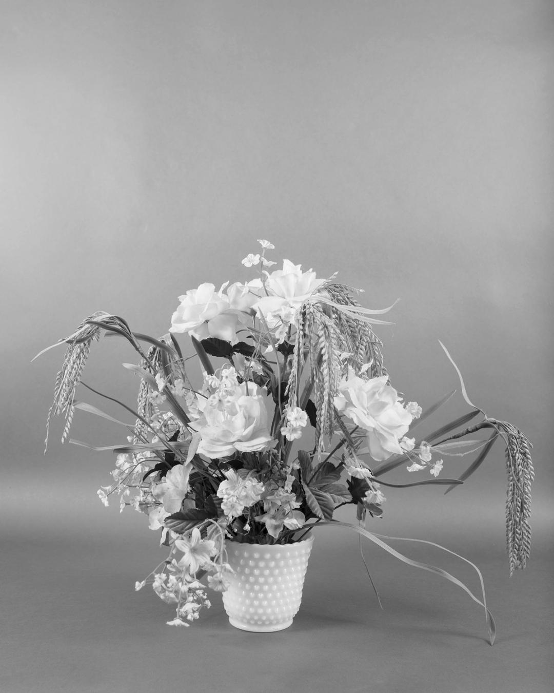 A black-and-white photo of a bouquet of artificial flowers, including bent wheat stalks.