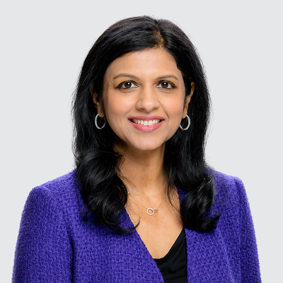 Headshot of a smiling woman with dark hair, wearing a purple jacket and hoop earrings.