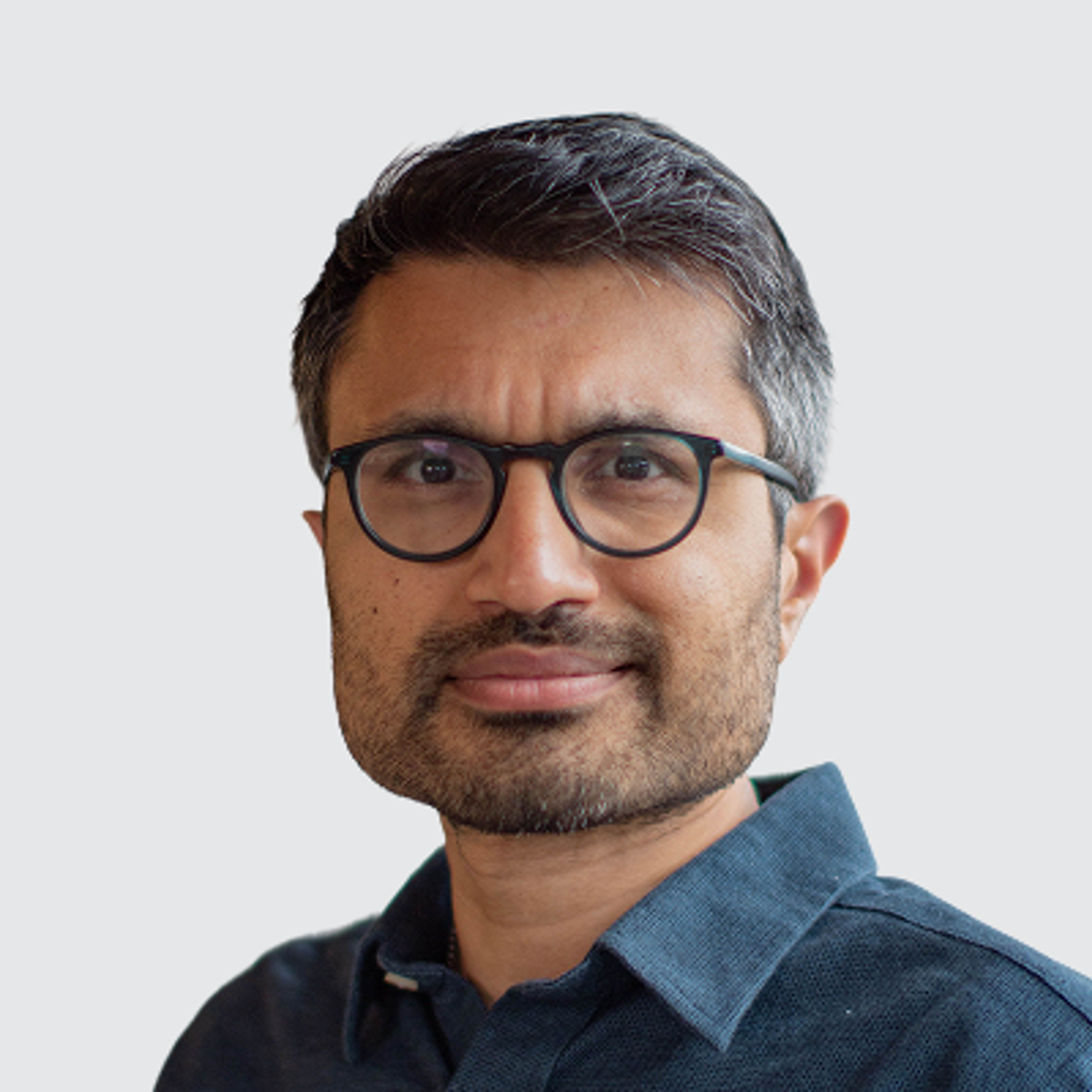 Headshot of a man with glasses and a beard, wearing a dark blue collared shirt.