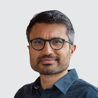 Headshot of a man with glasses and a beard, wearing a dark blue collared shirt.