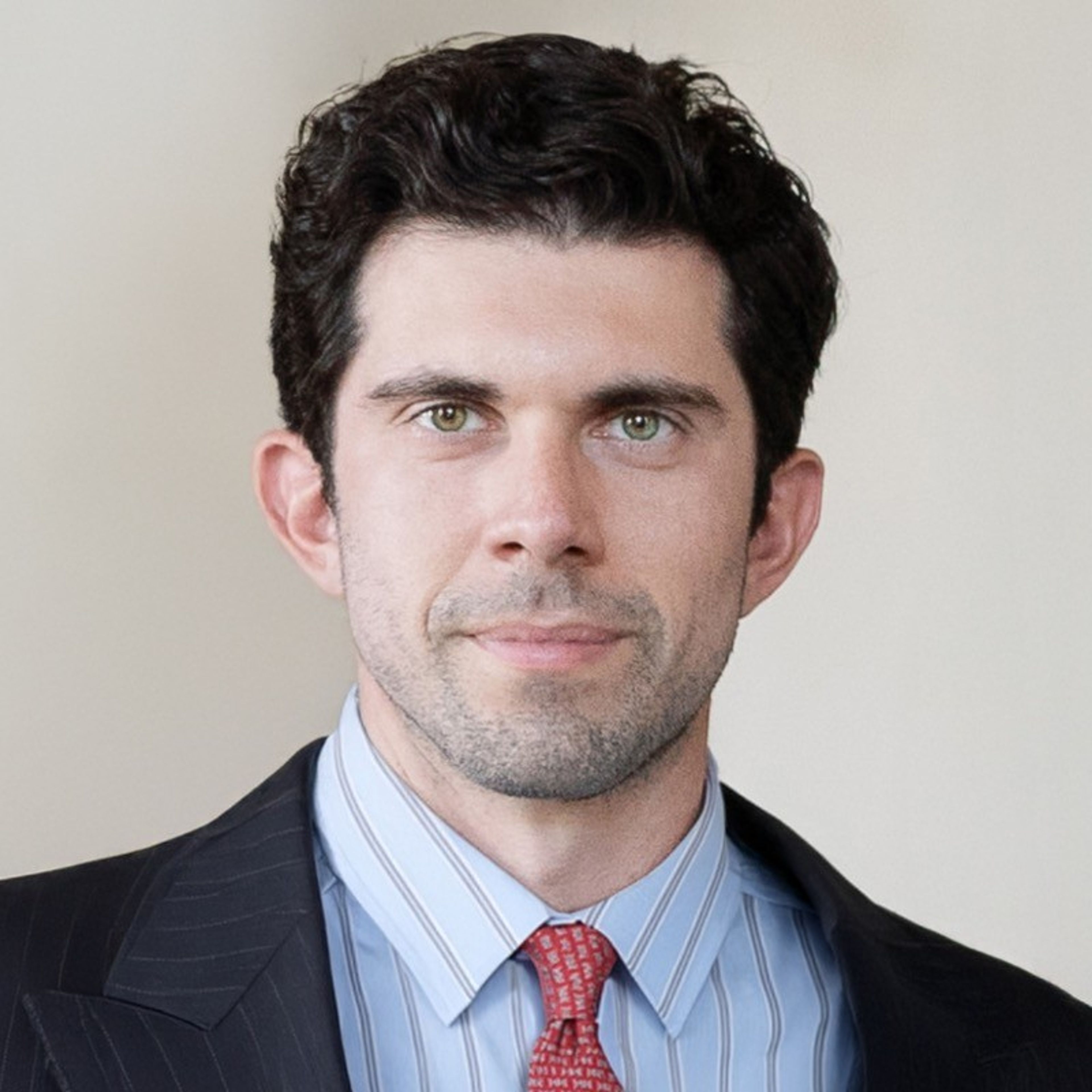 Portrait of a man with dark hair, green eyes, and stubble, wearing a suit and tie.