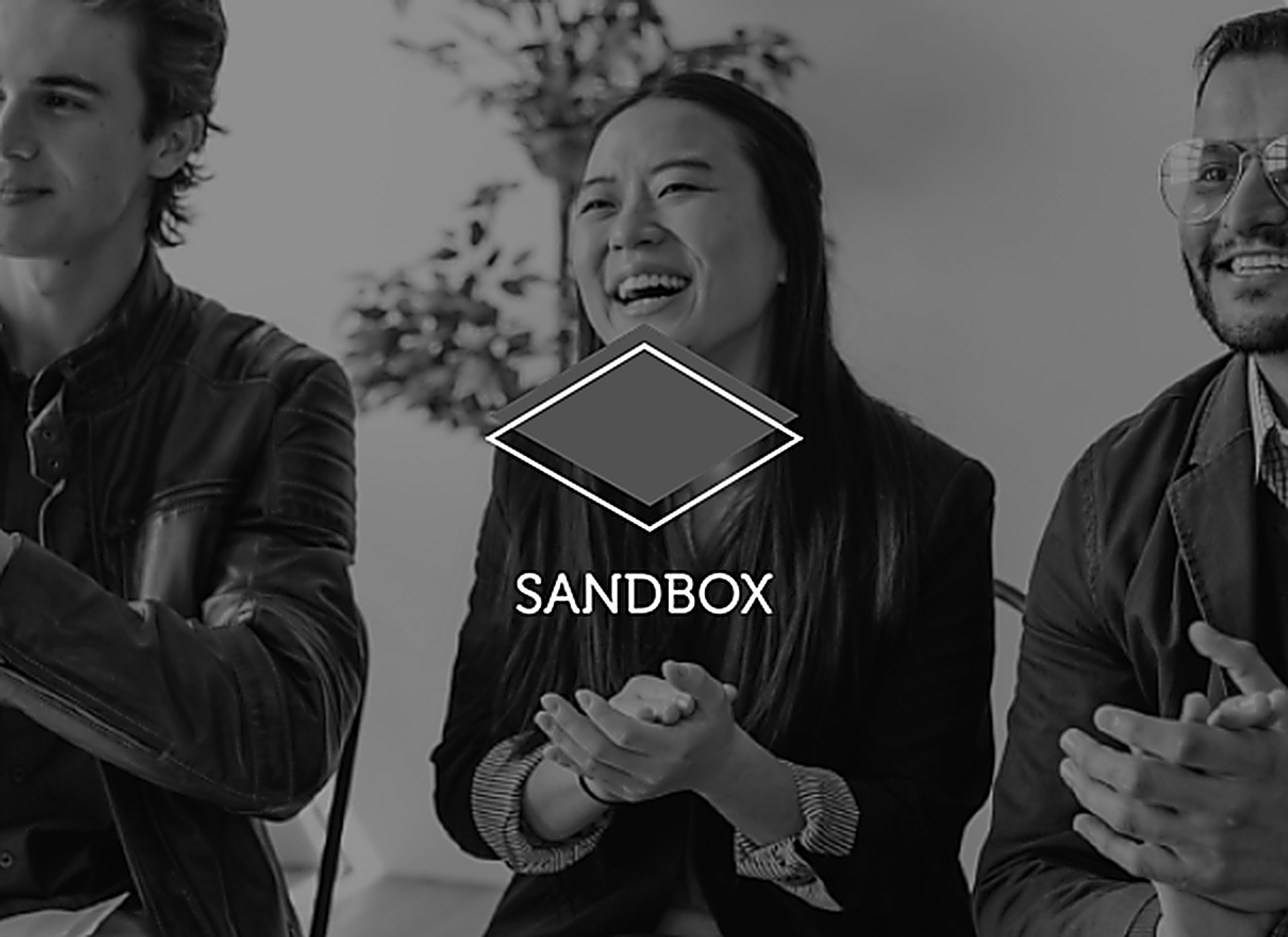 a black and white photo of three people with the sandbox logo behind them