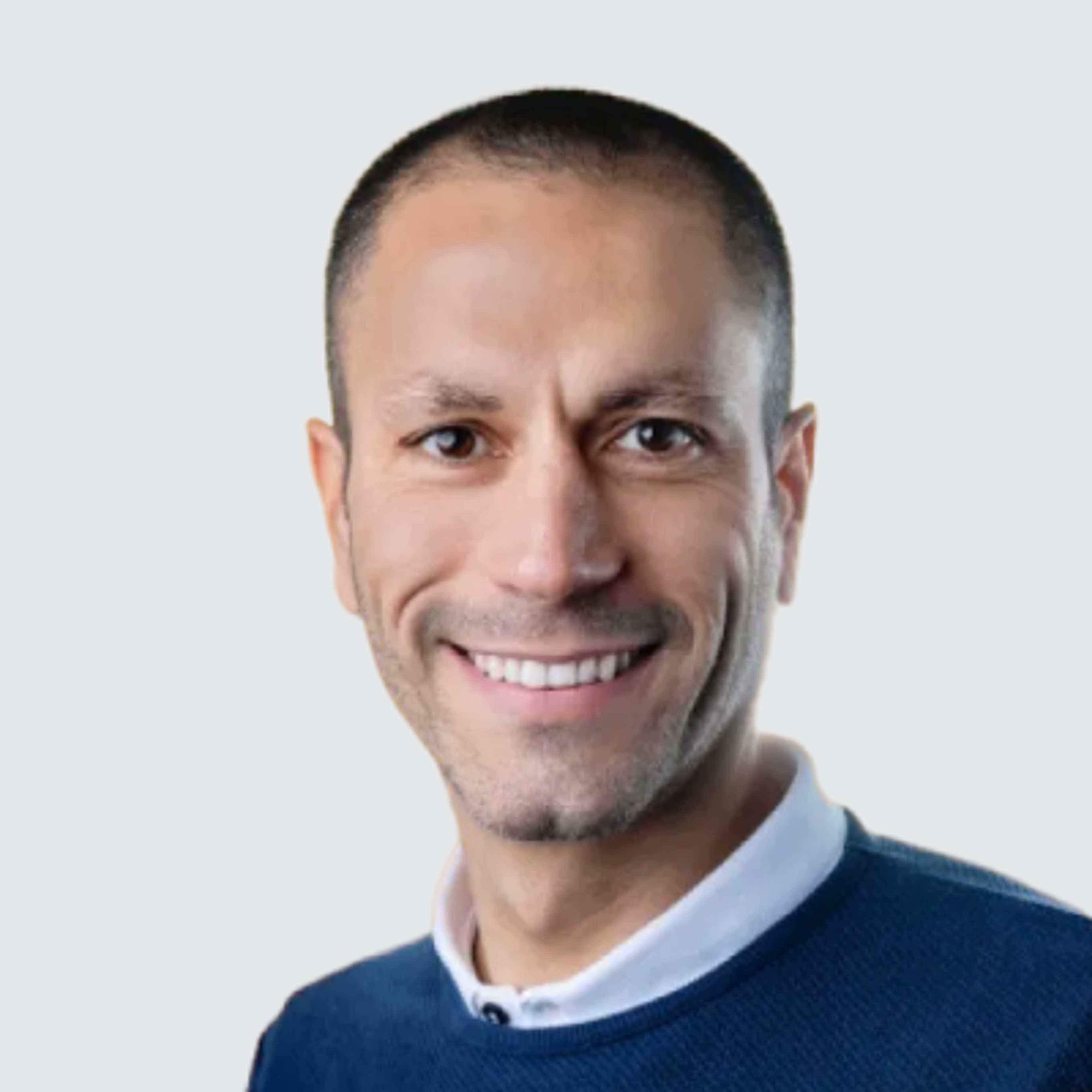 Headshot of a smiling man with short dark hair in a blue sweater.