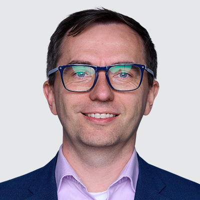 Headshot of a smiling man wearing blue-framed glasses and a blue suit jacket.