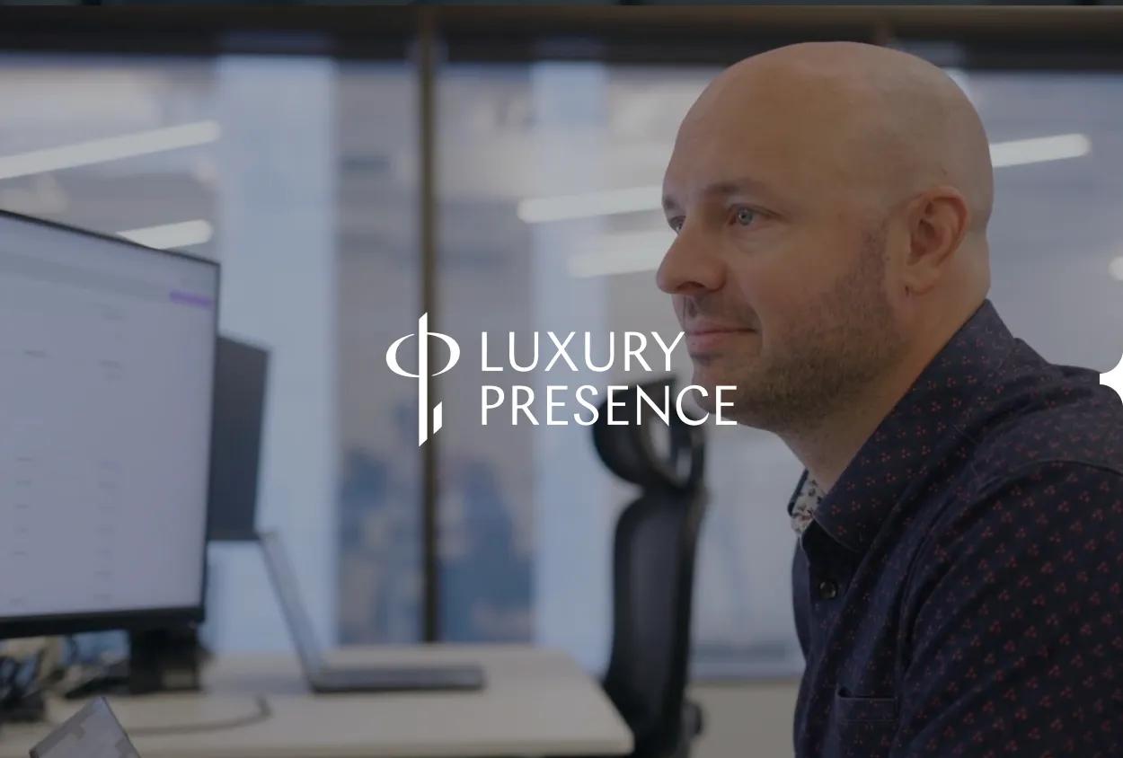 A man with a beard and shaved head in an office, with the 'Luxury Presence' logo overlaid.