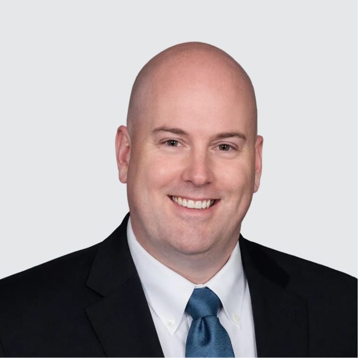 A smiling bald man in a dark suit and blue tie.