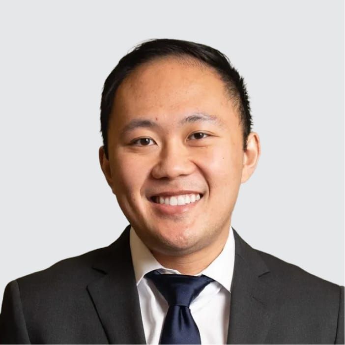Headshot of a smiling Asian man in a suit and tie.