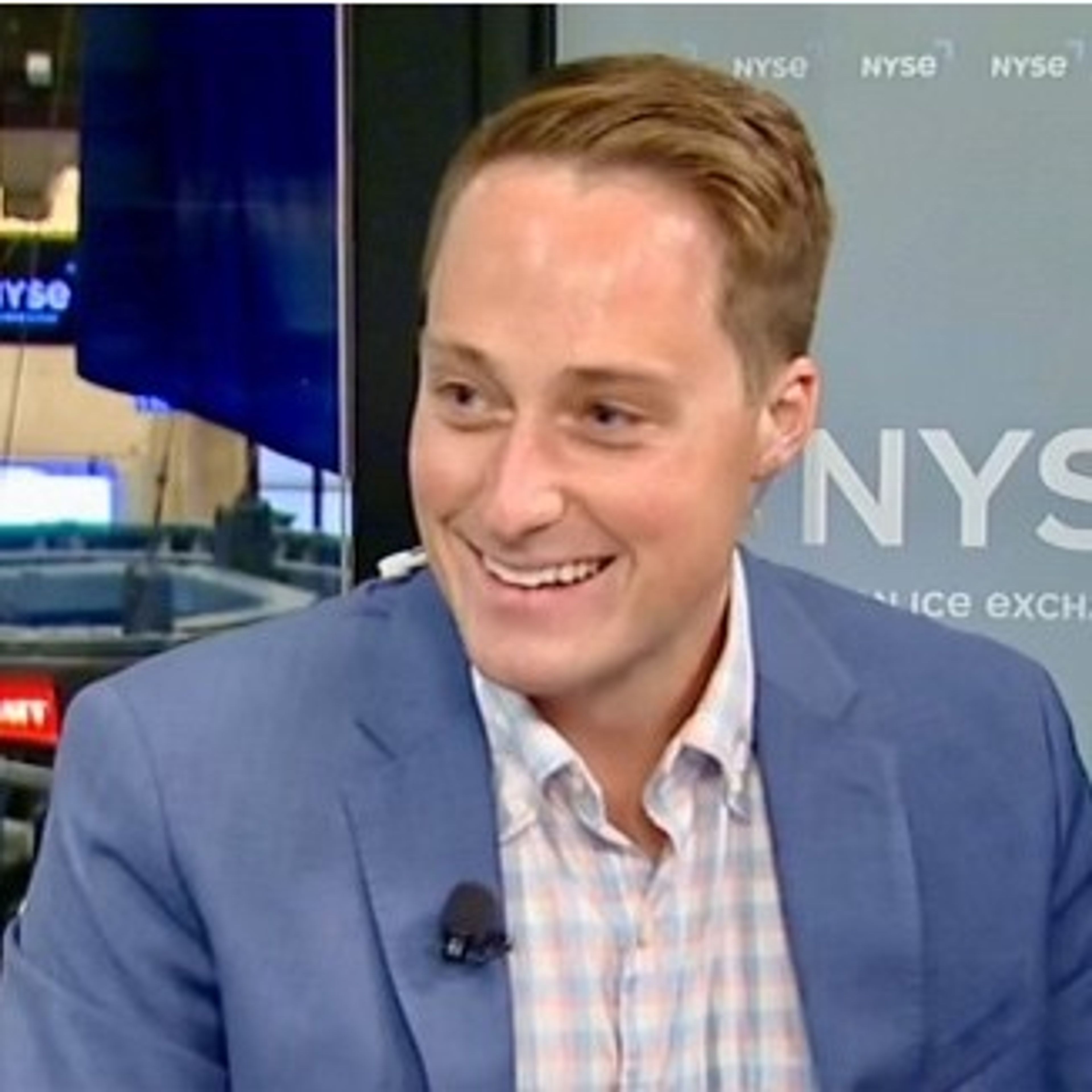 a man in a suit and plaid shirt is smiling while sitting in front of a television 