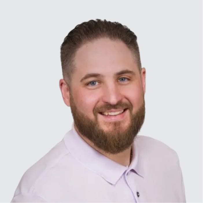 Headshot of a smiling man with a beard and light purple polo shirt.