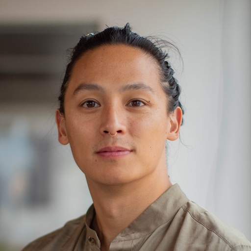 Close-up of a man with dark hair pulled back, a septum piercing, and an olive shirt.