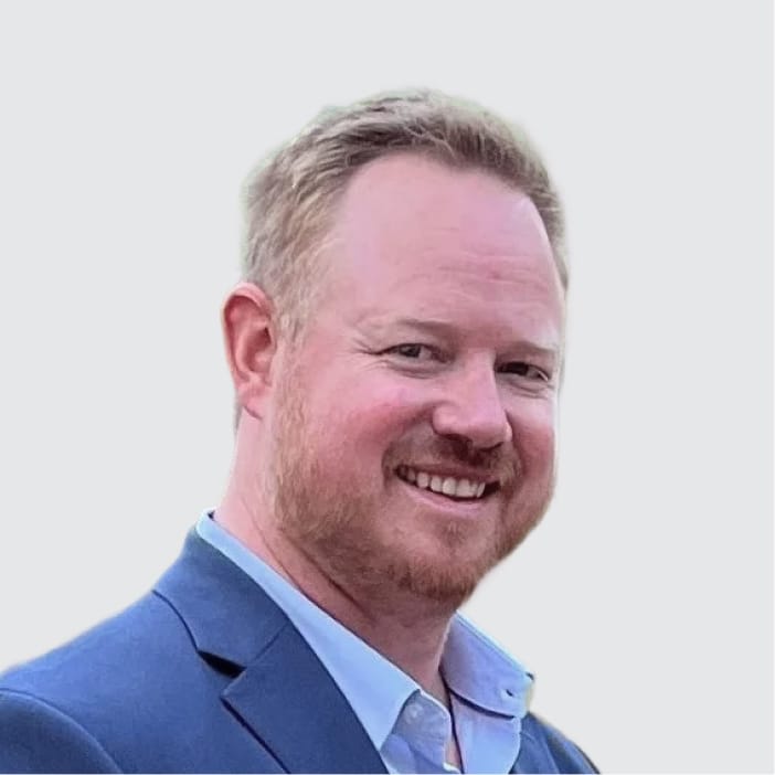 Smiling man with reddish-blonde hair and beard wearing a blue suit jacket.