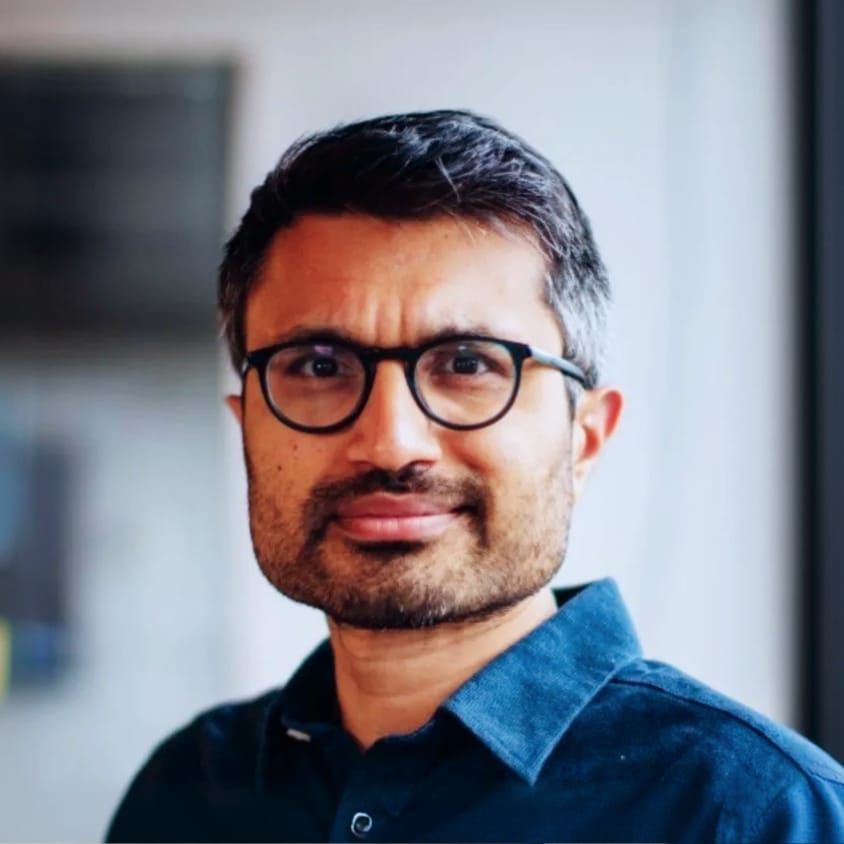 Headshot of a man with dark-rimmed glasses and a beard, smiling slightly.
