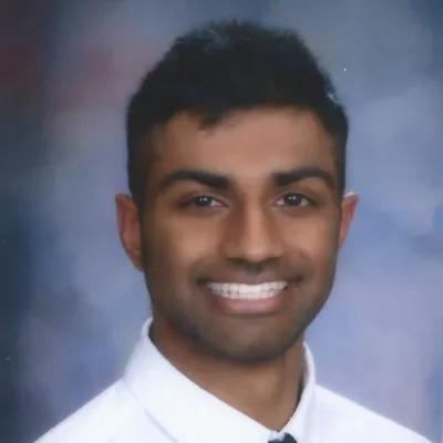 Headshot of a smiling young man with dark hair and a light complexion, wearing a white shirt and tie against a blue background.