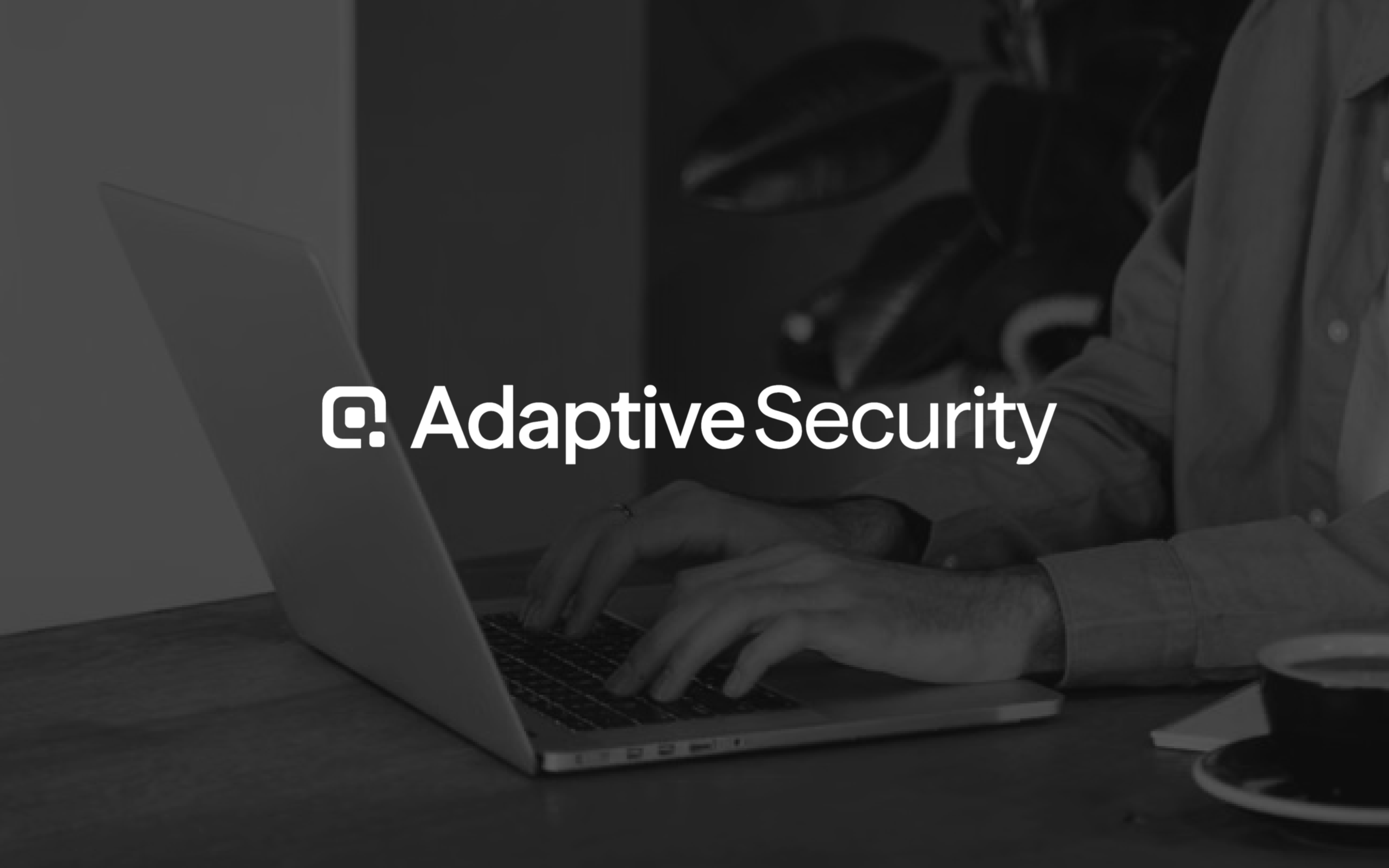 AdaptiveSecurity logo over a grayscale image of a person typing on a laptop.