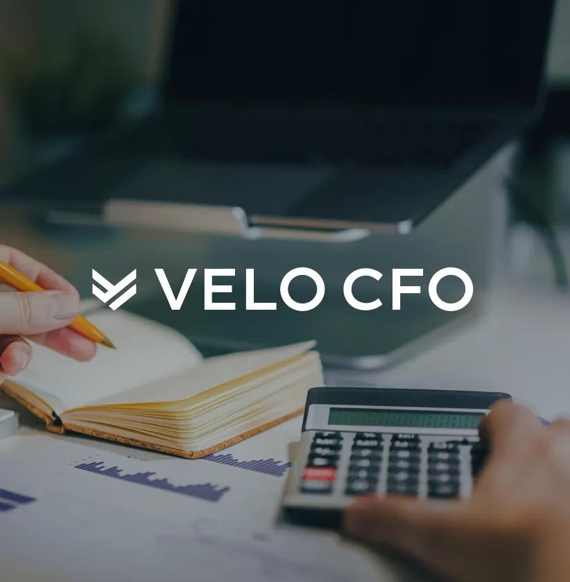 VELO CFO logo over a person working with a calculator, notebook, and laptop.