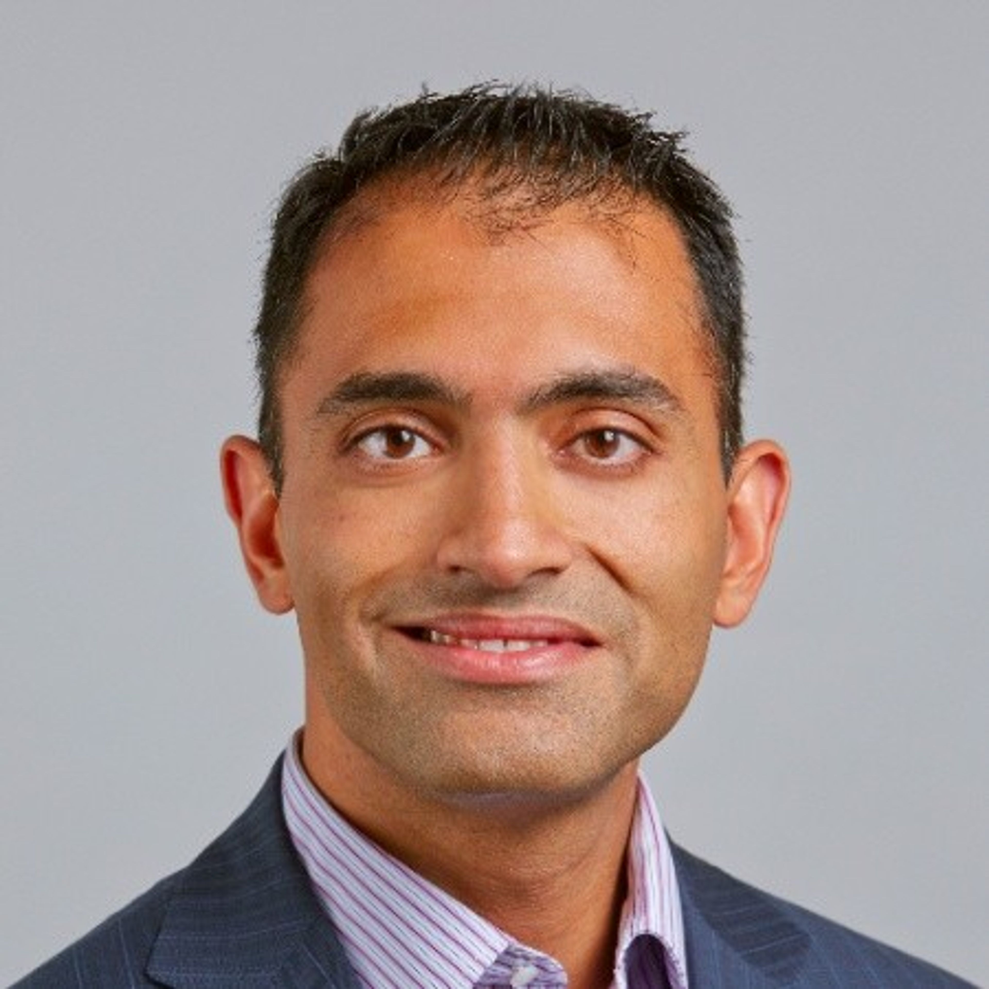 Headshot of a smiling man with dark hair in a suit.