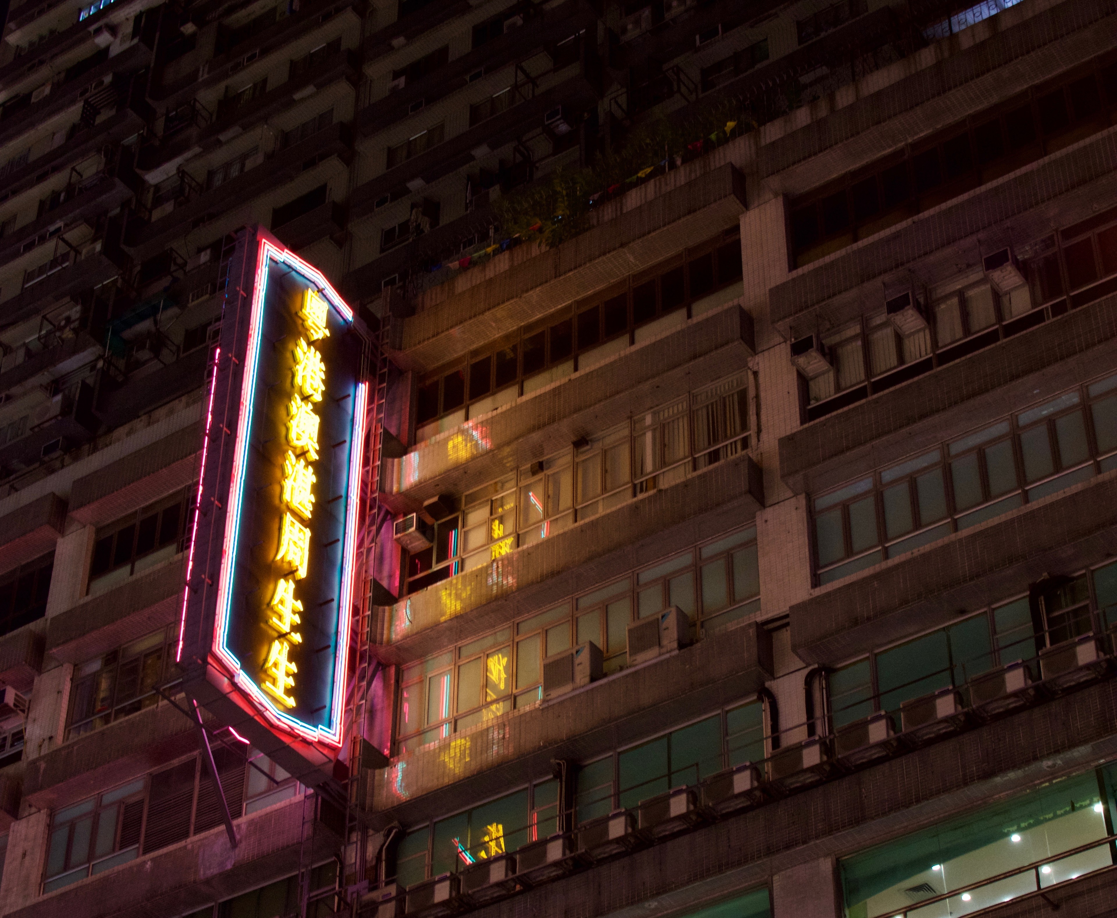 A narrow illuminated sign rises along the façade of an older apartment building.