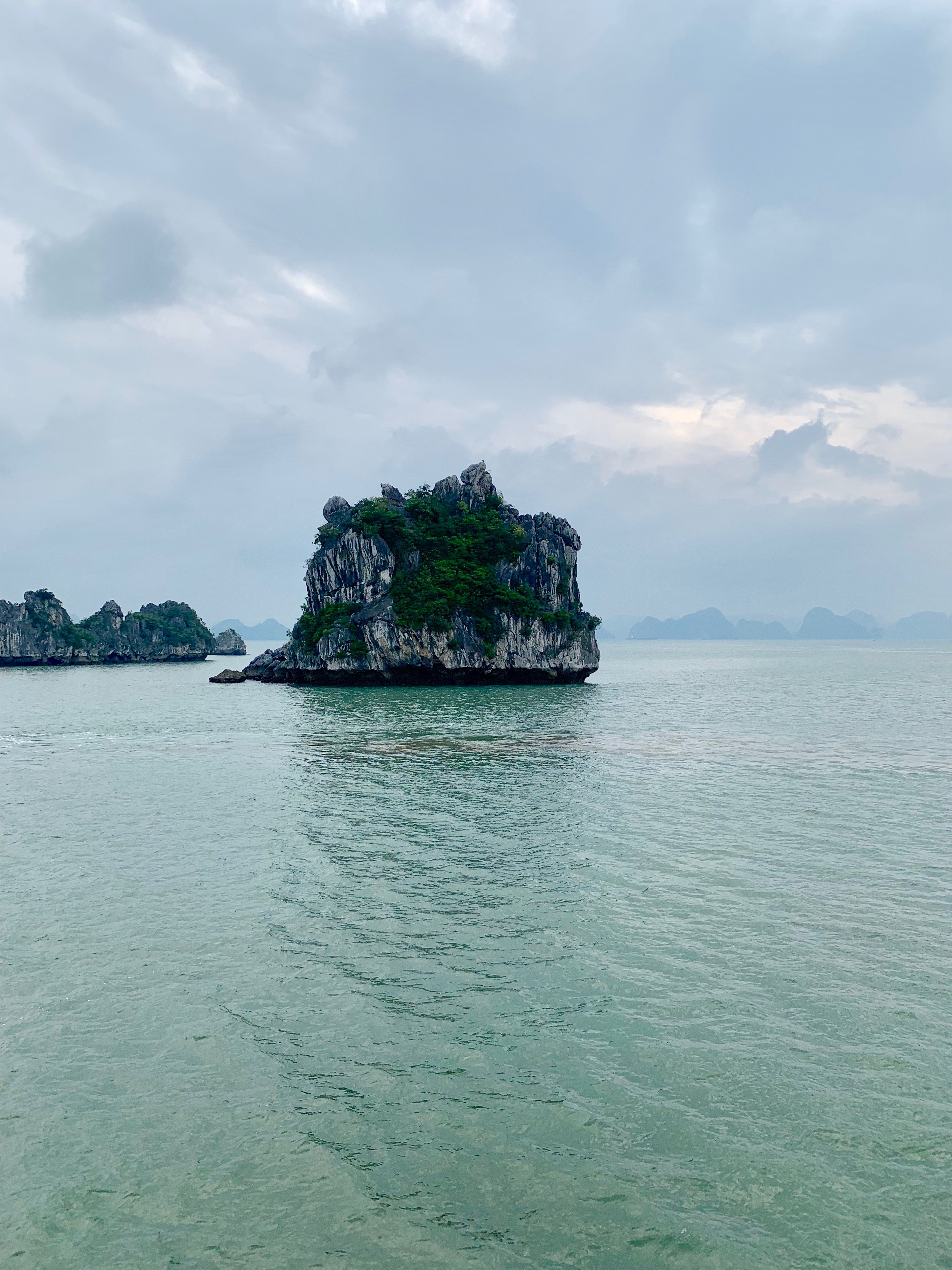 A small limestone island stands alone in calm water beneath an overcast sky.