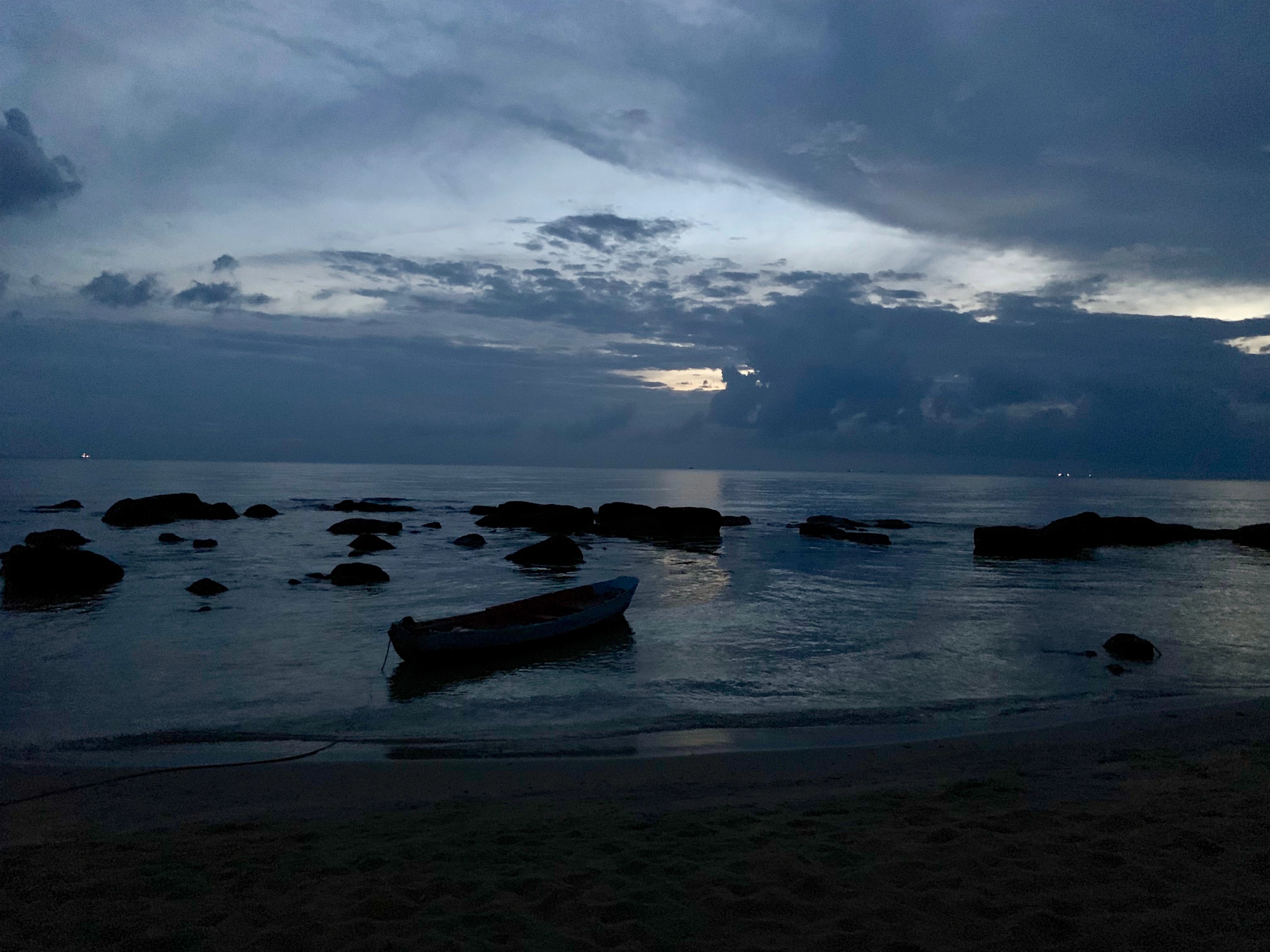 A small boat rests on dark water near a rocky shoreline beneath cloudy twilight.