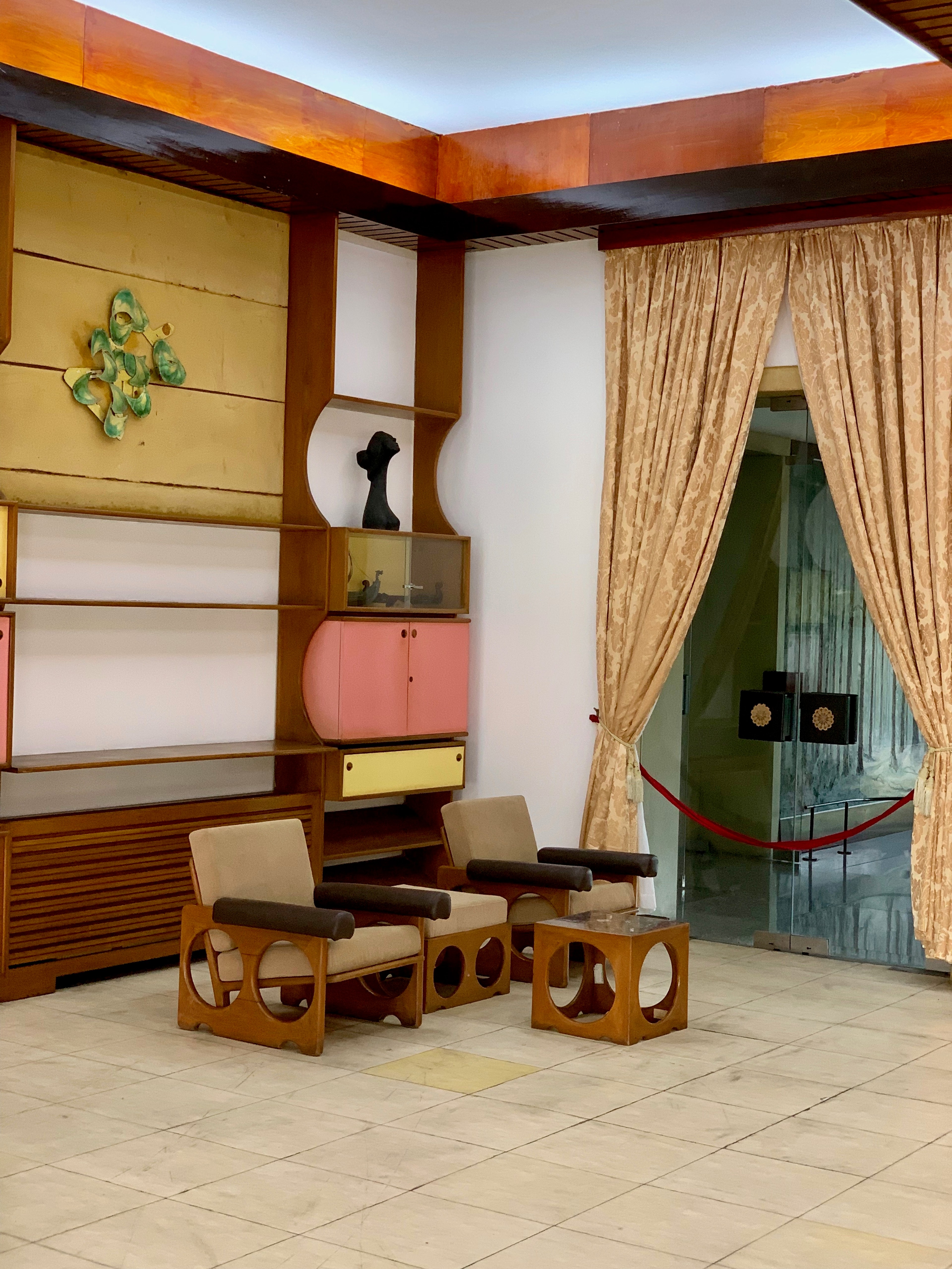 A warmly lit room is furnished with wooden chairs, a low table, and curtains.