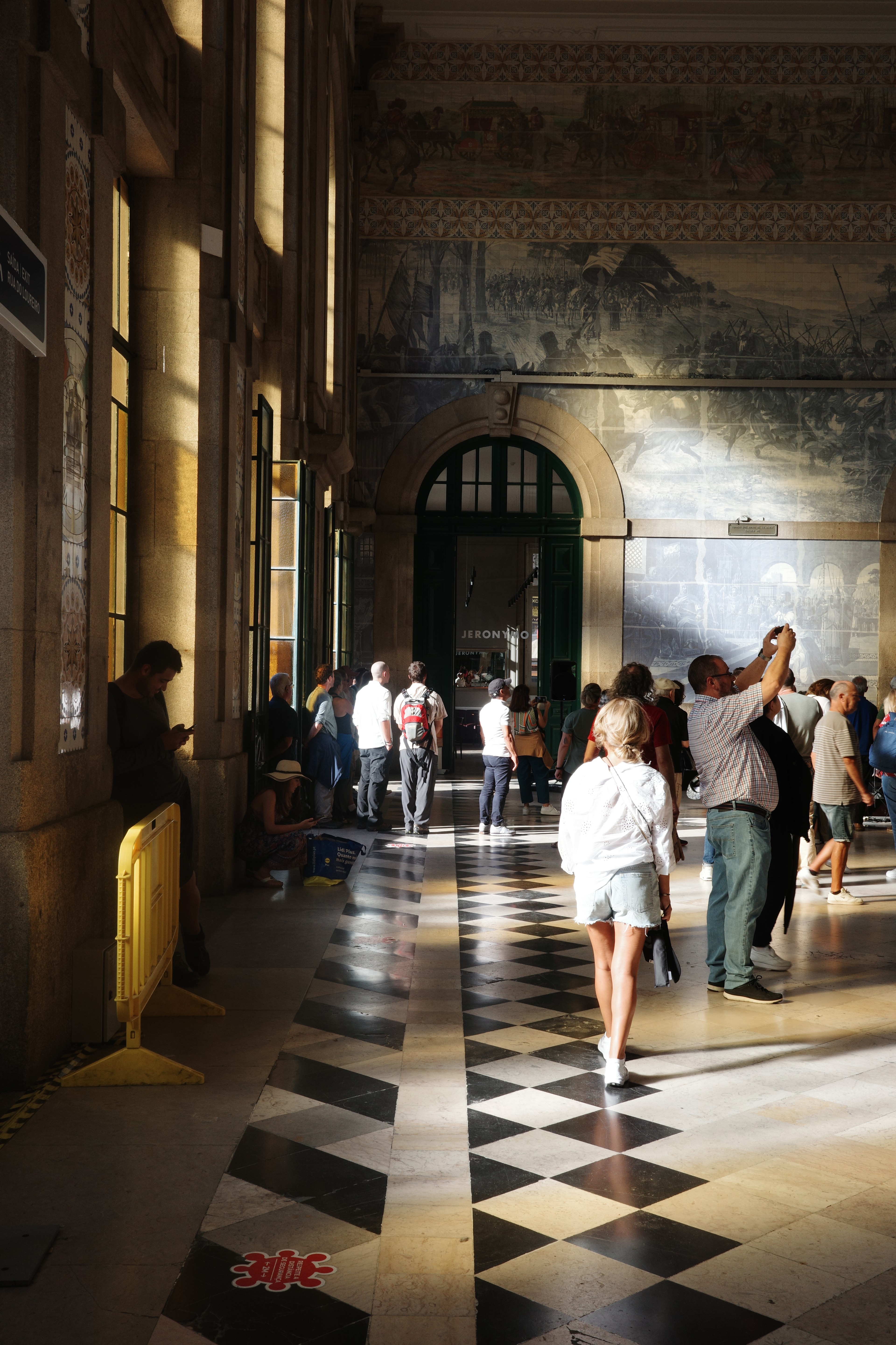 Visitors walk through an ornate hall with a black-and-white tiled floor.