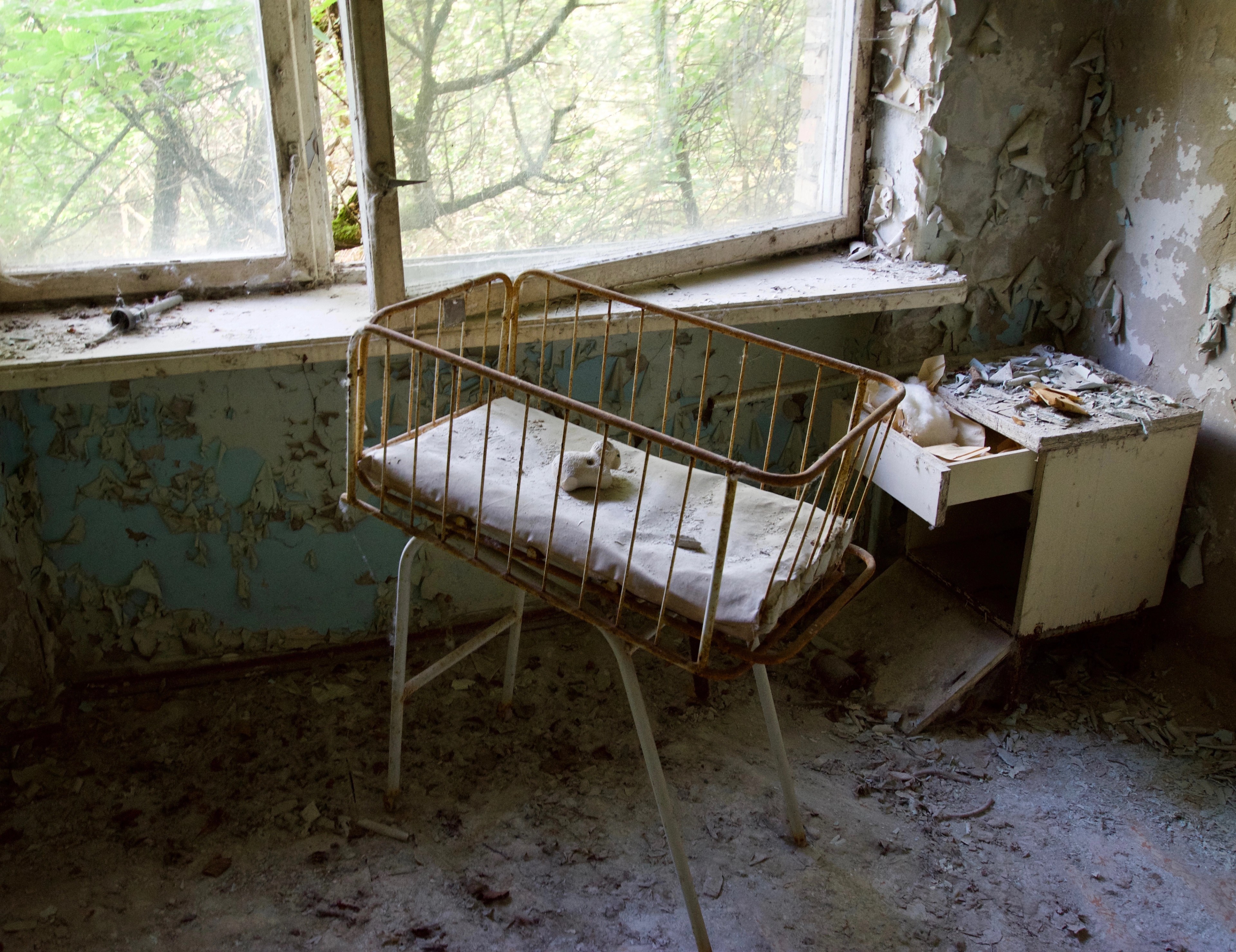 A metal bed stands beside a broken window.
