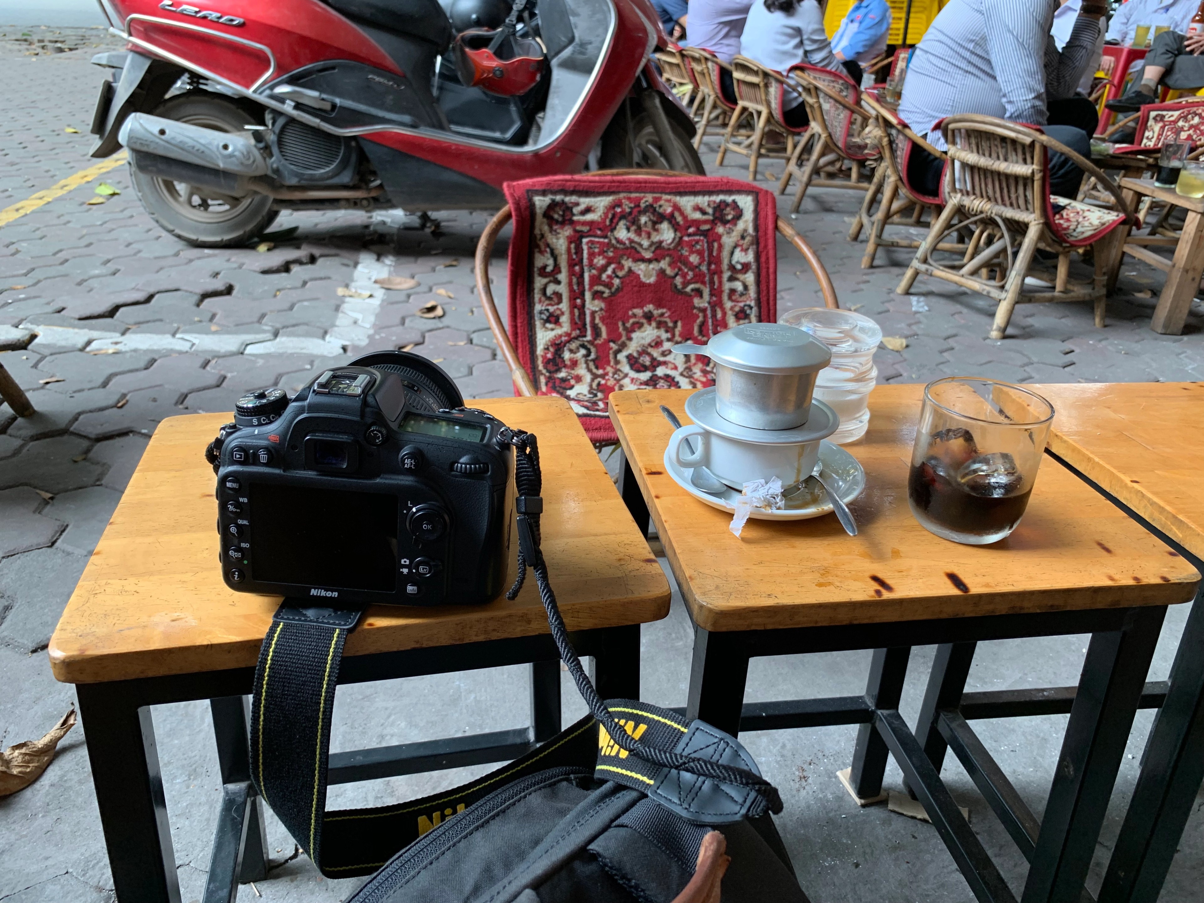 A cup of coffee and a camera sit on a small outdoor café table.