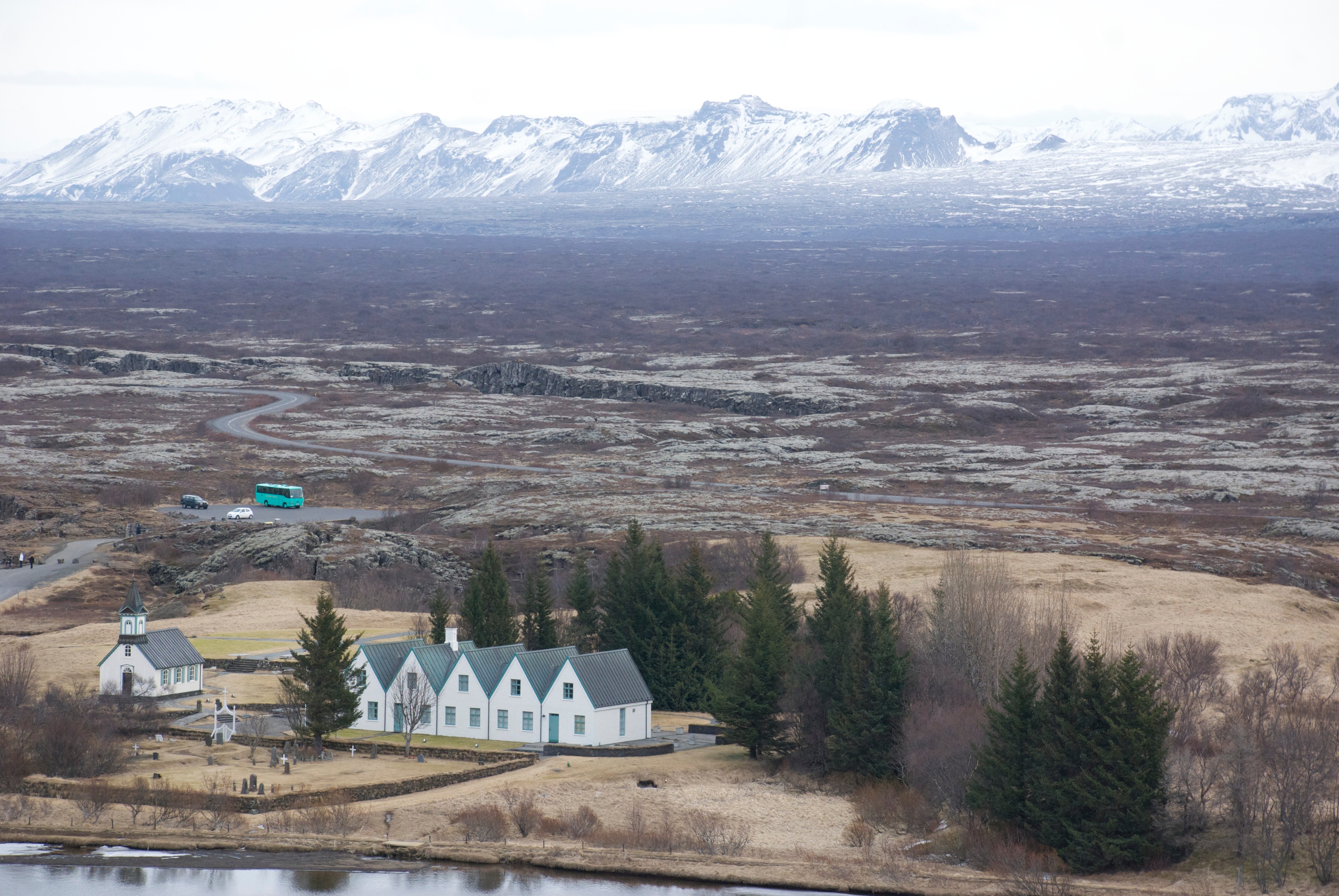A small white church and houses stand below a snow-covered mountain range.