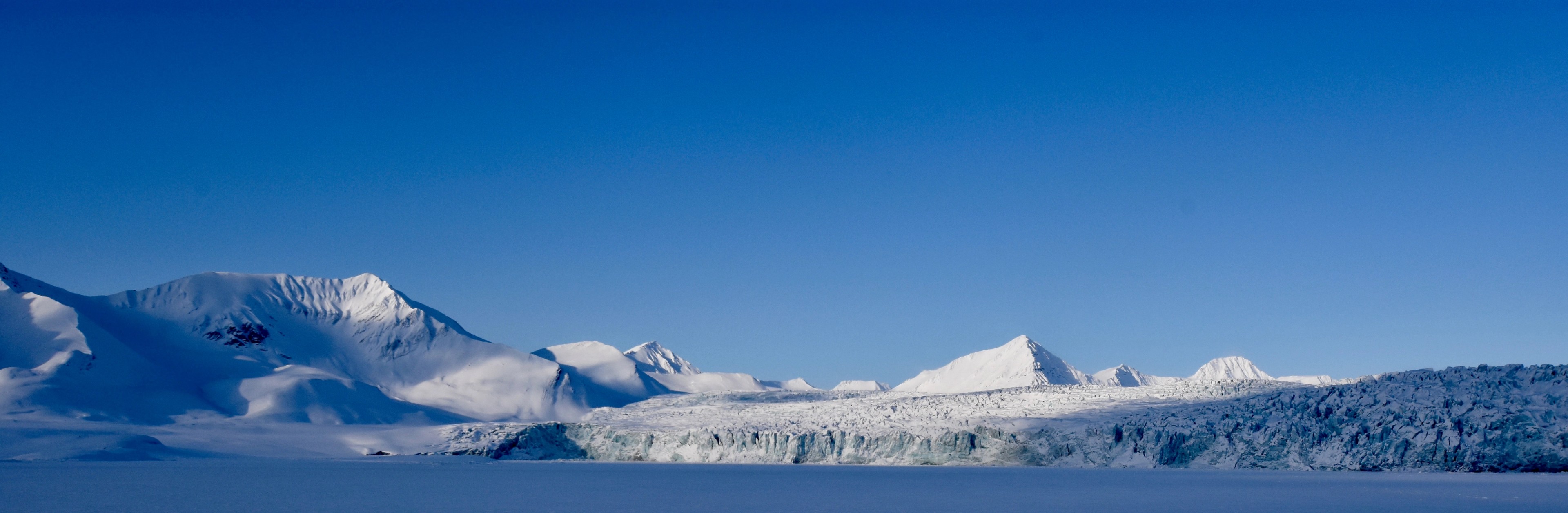 A panoramic view of a snowy mountain range beneath a blue sky.