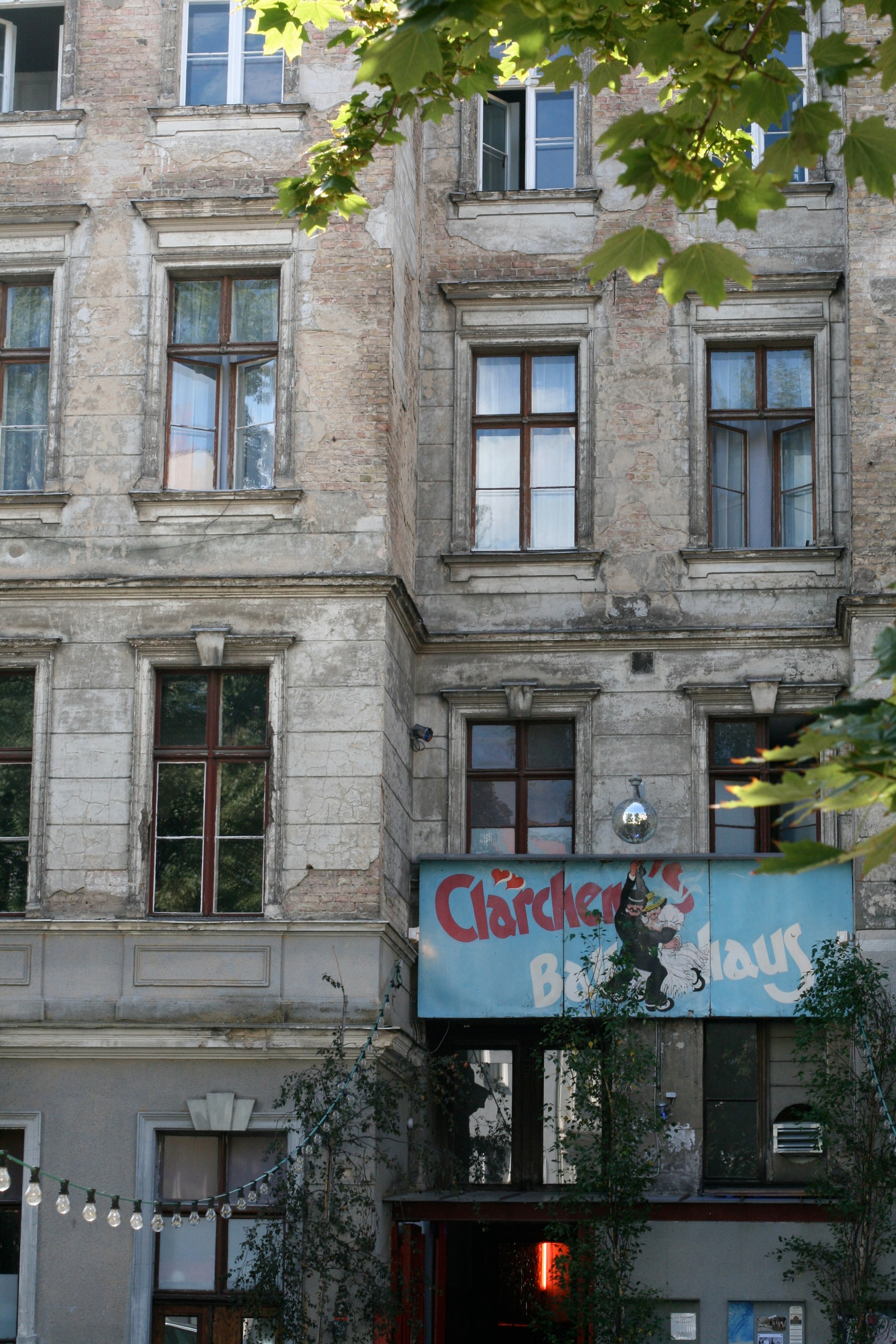 A weathered apartment façade with balconies and a partly obscured street sign.