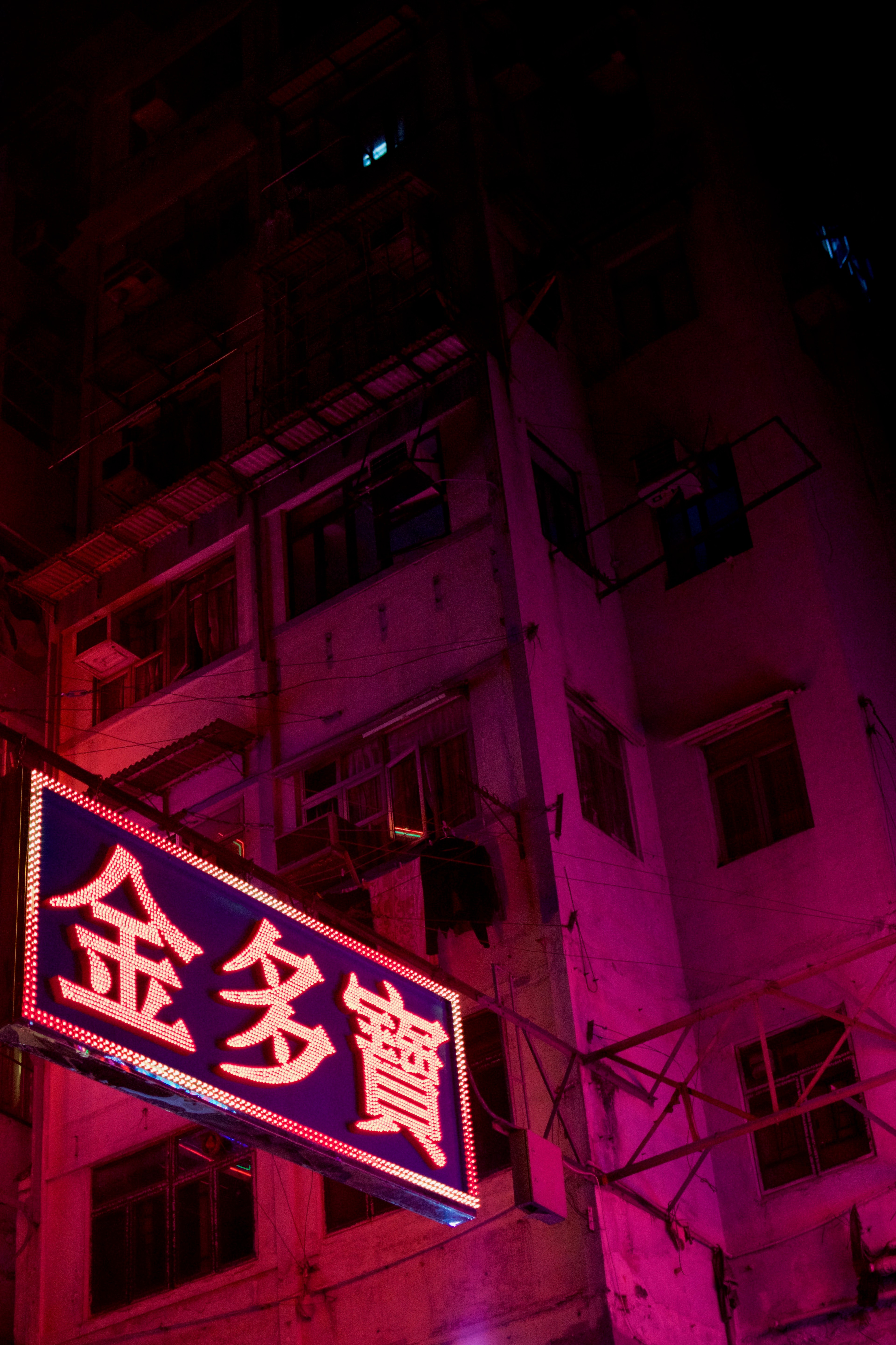 A narrow pink-lit sign projects from a building at night.