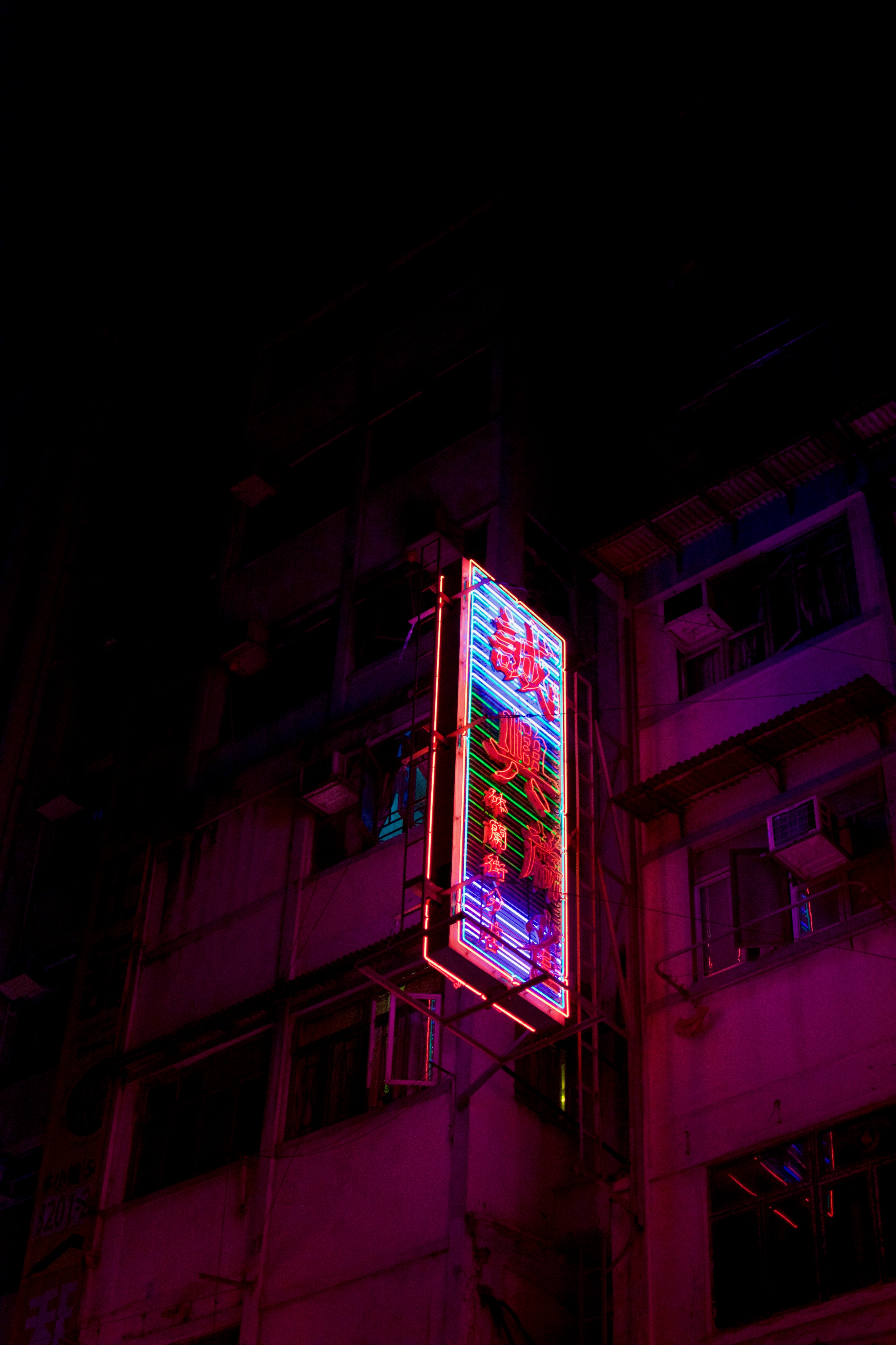 A vertical blue and red neon sign hangs between tall buildings.