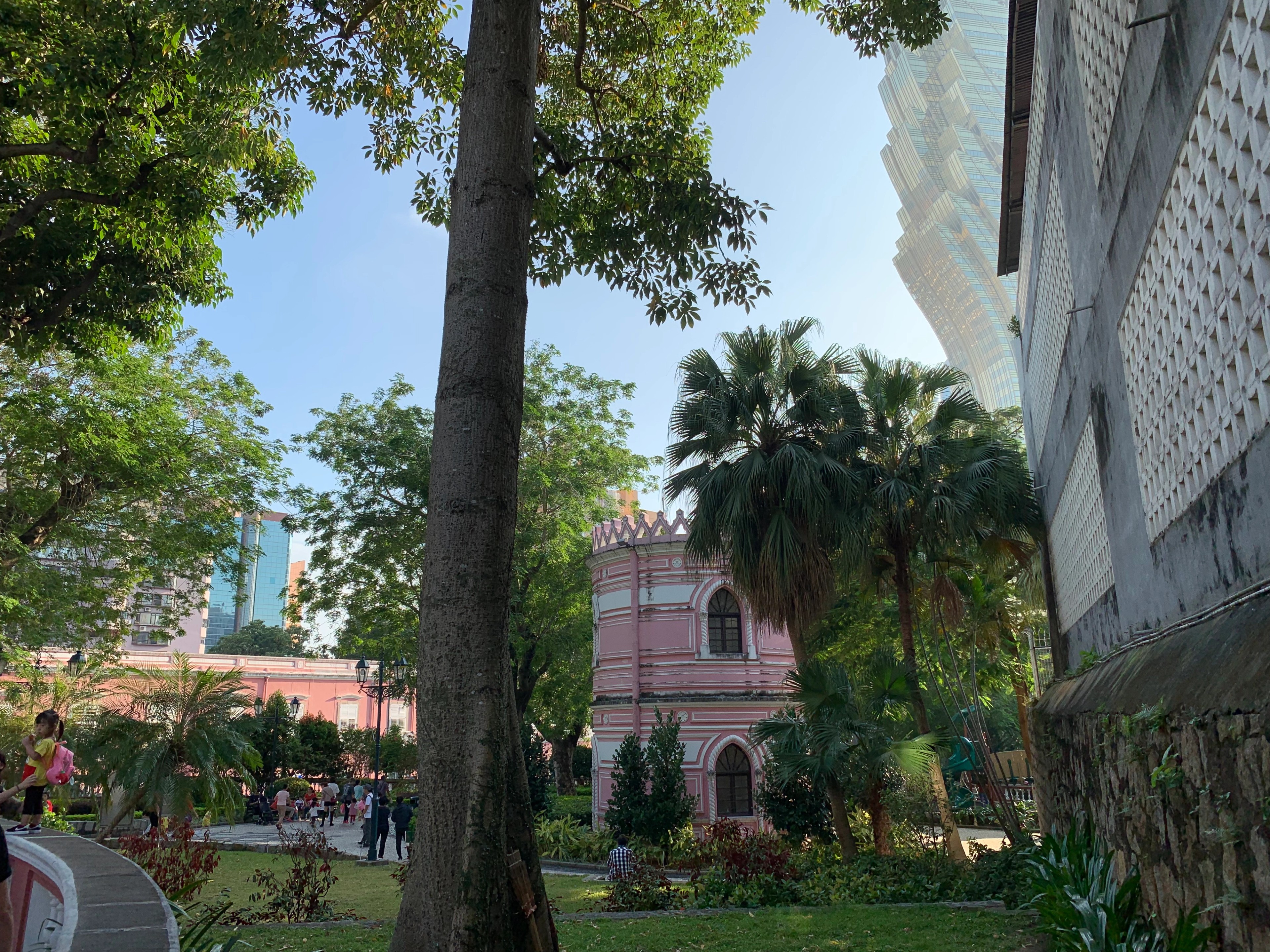 Pink historic building and park beneath leafy trees in Macau.