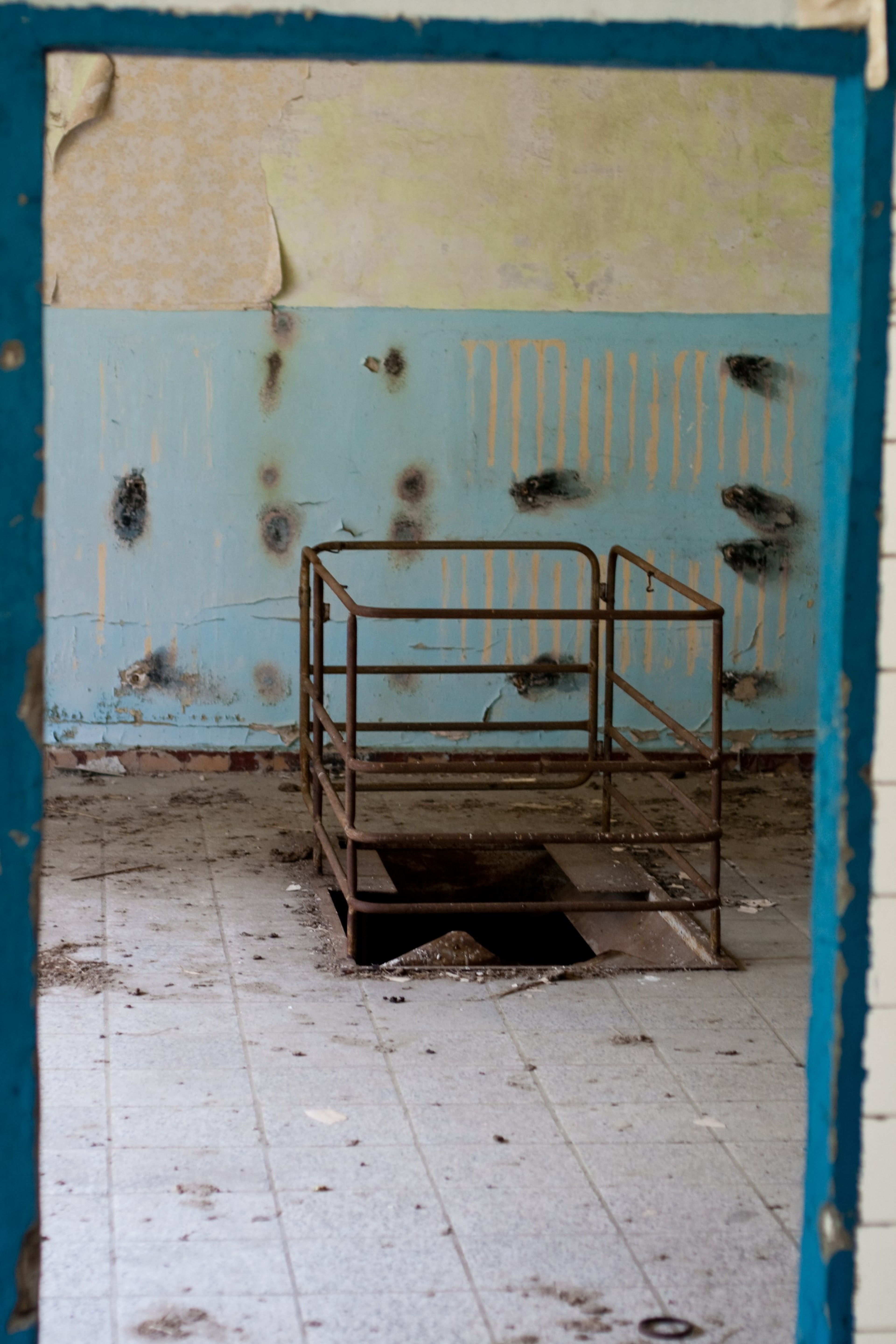 A rusty metal bed frame sits in a bare, worn room.