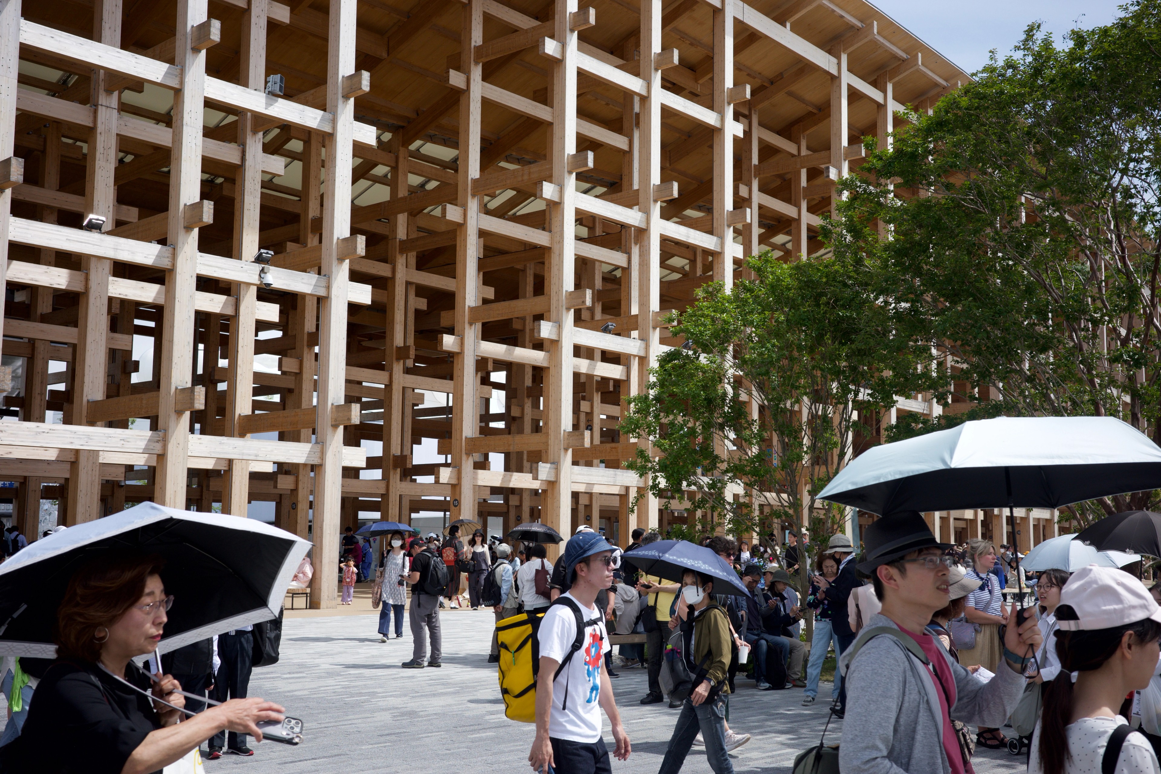 Visitors with umbrellas gather before a large timber structure.