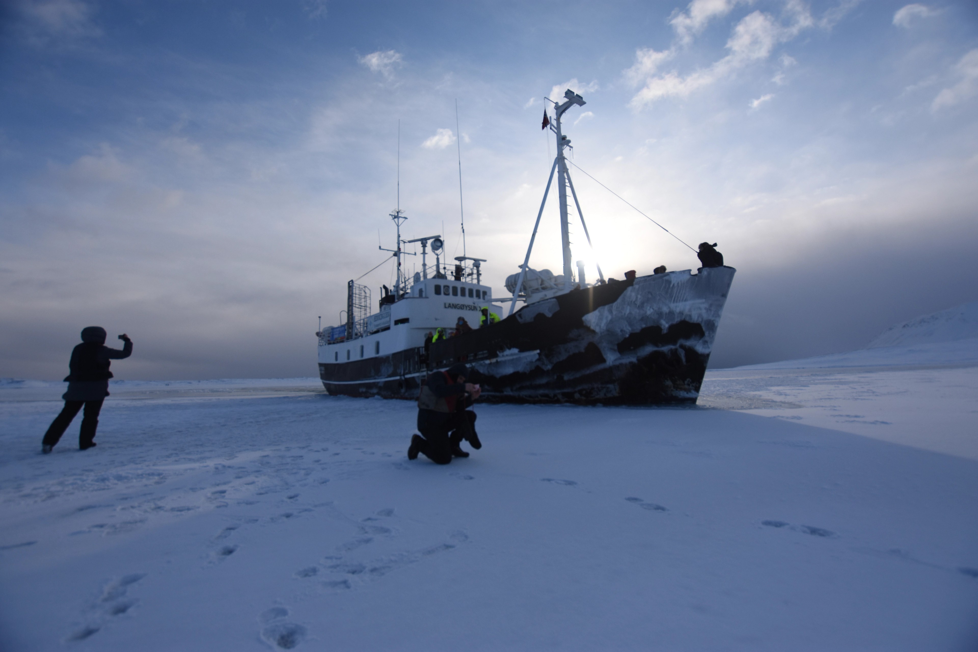 A ship rests on snow beside a mountain range.