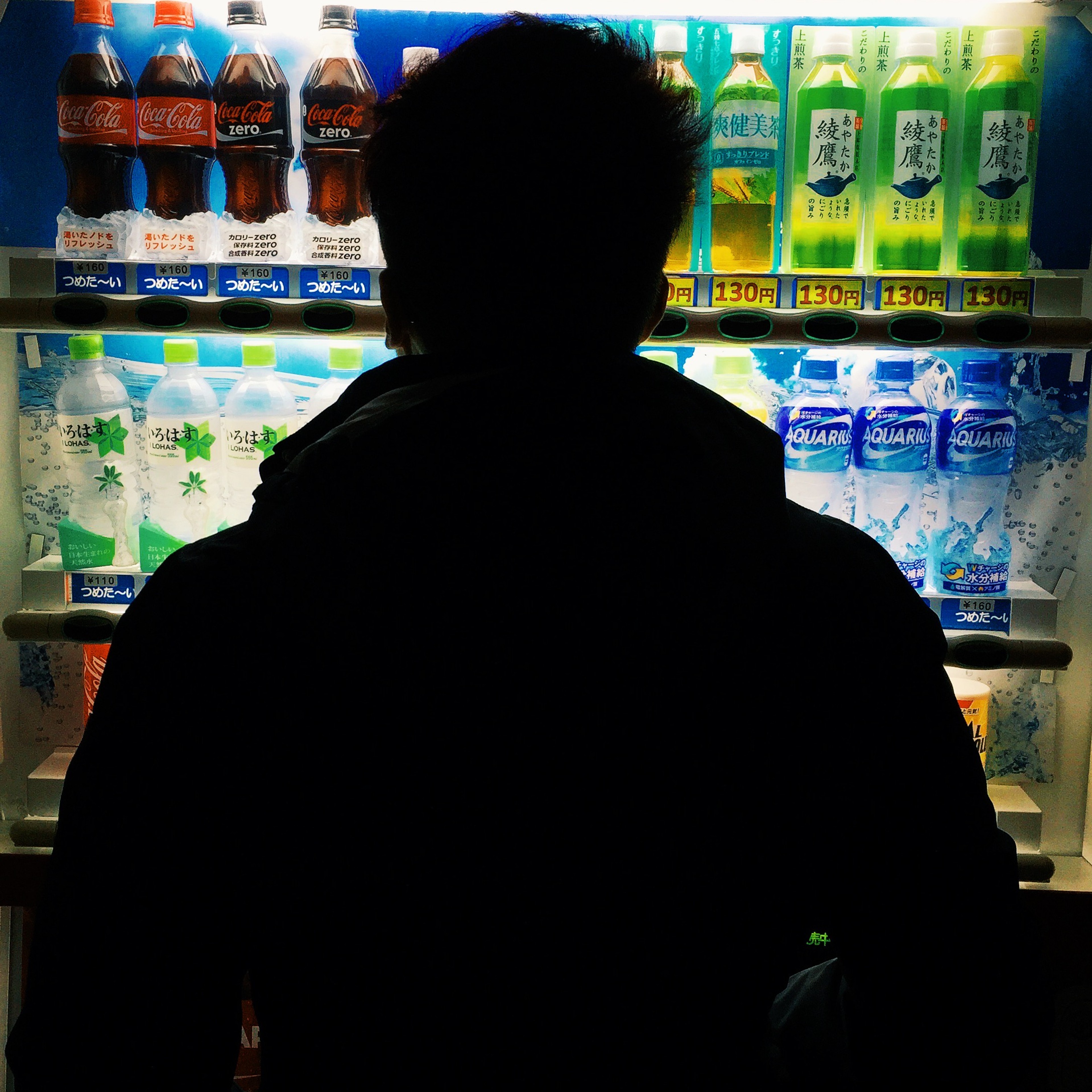 A person stands silhouetted before a brightly lit row of vending machines.