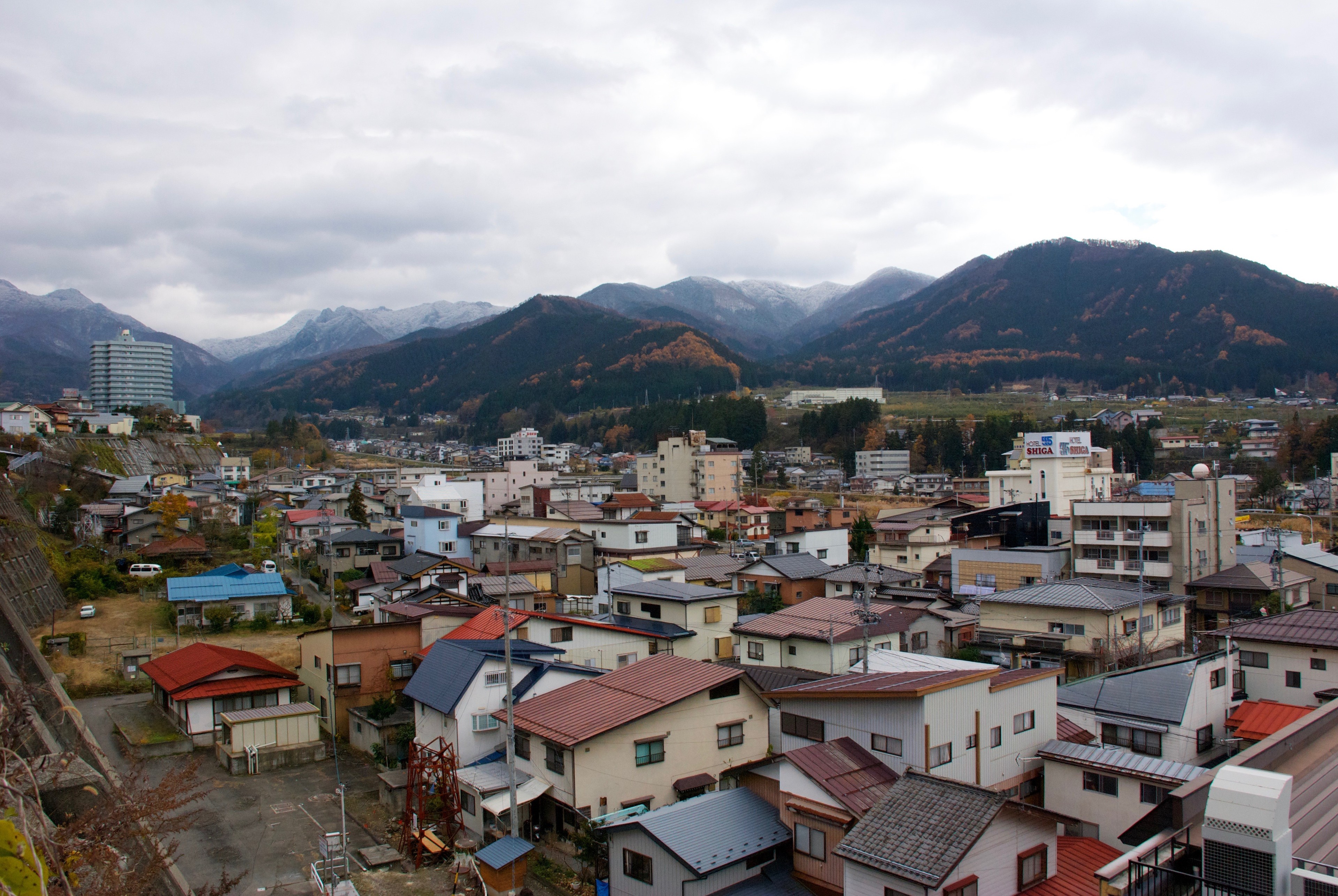 A Japanese town spreads across a valley below a cloud-covered mountain.
