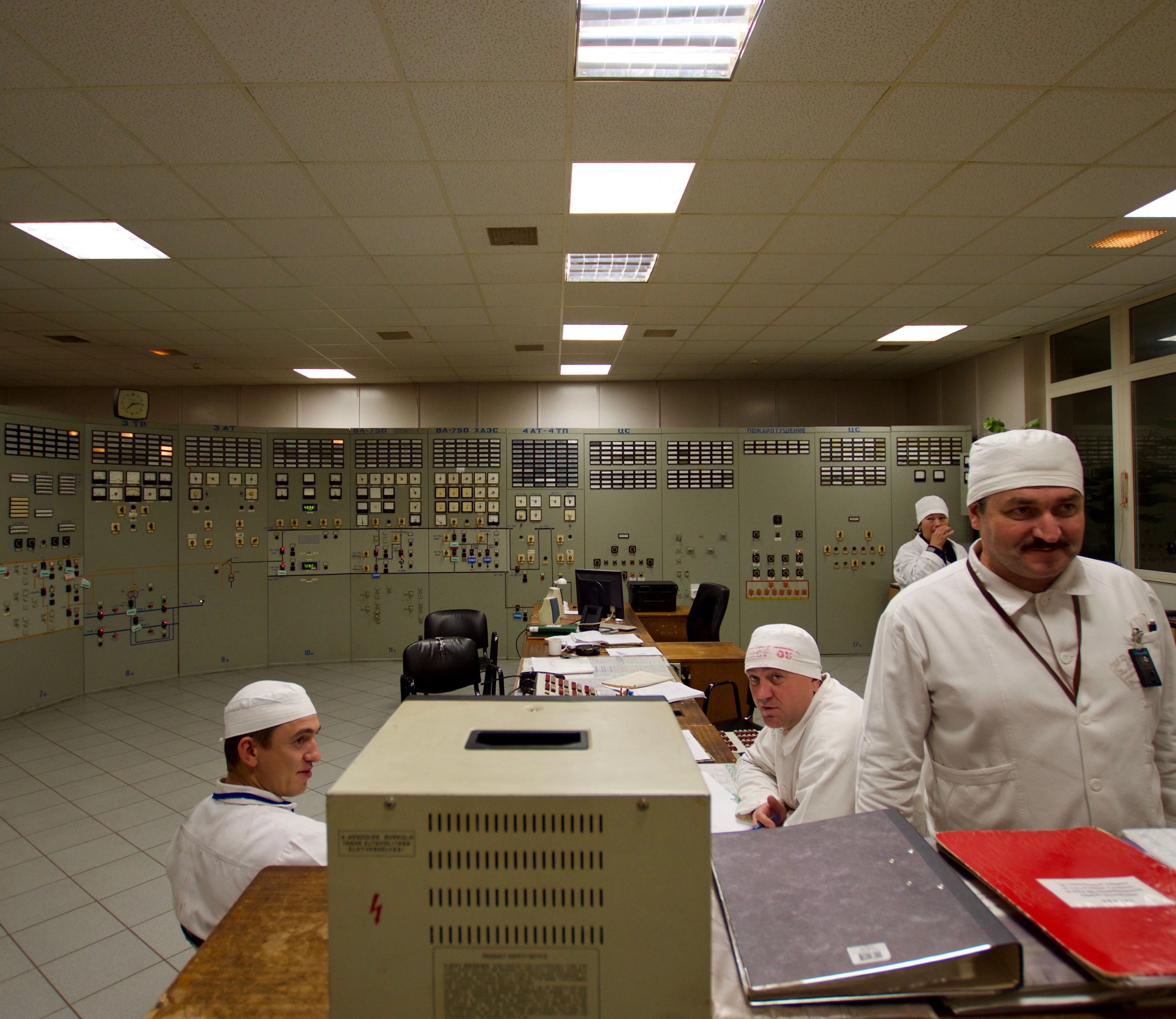 Workers in white uniforms stand in a control room.